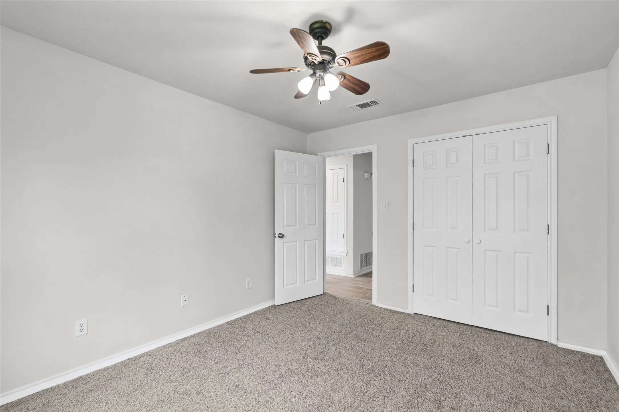 Carpeted bedroom with a ceiling fan light fixture, two-panel closet doors, and white trim