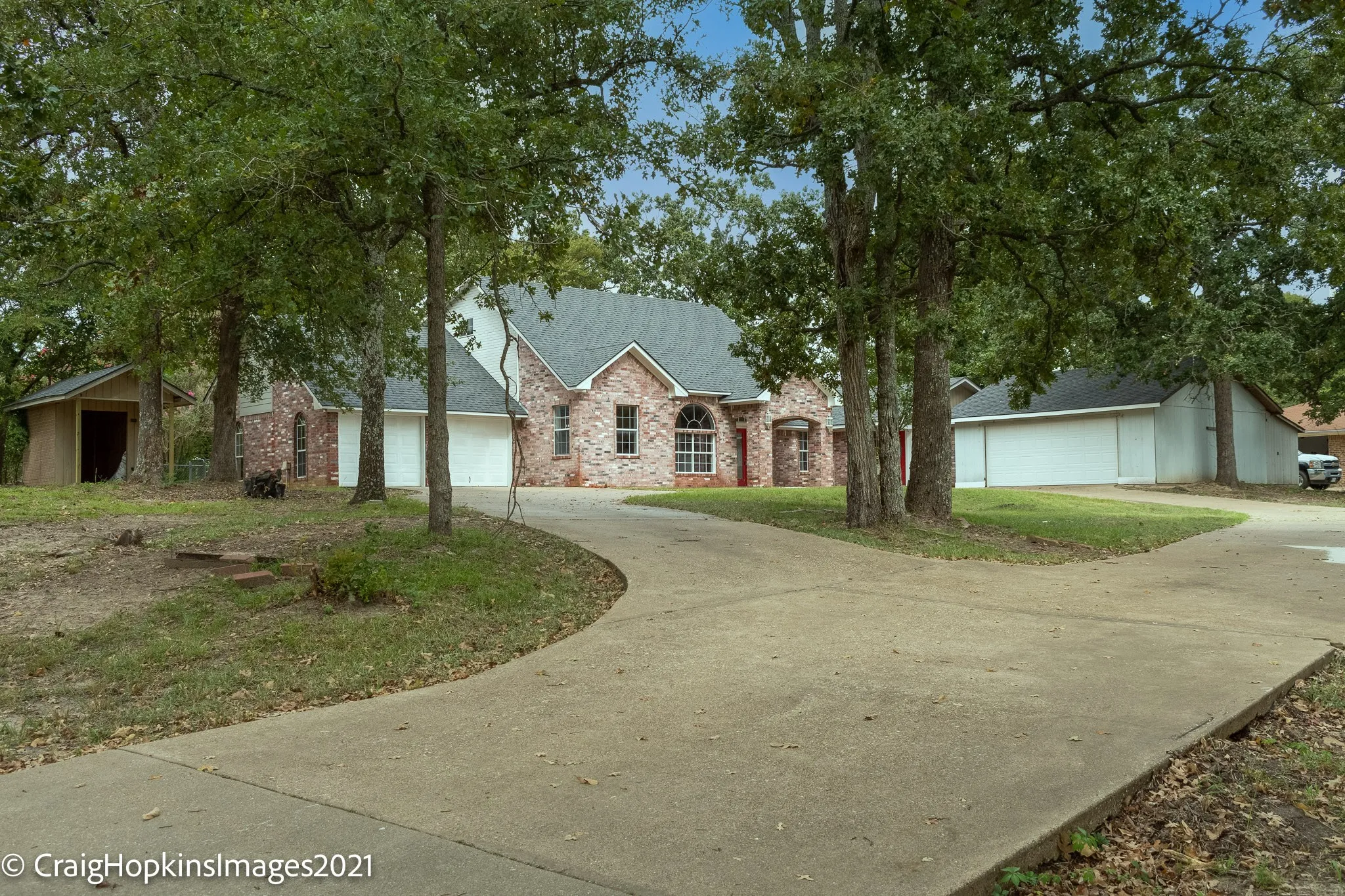 Brick and siding exterior residence featuring a curved concrete driveway, attached two-car garage, and a separate detached garage structure