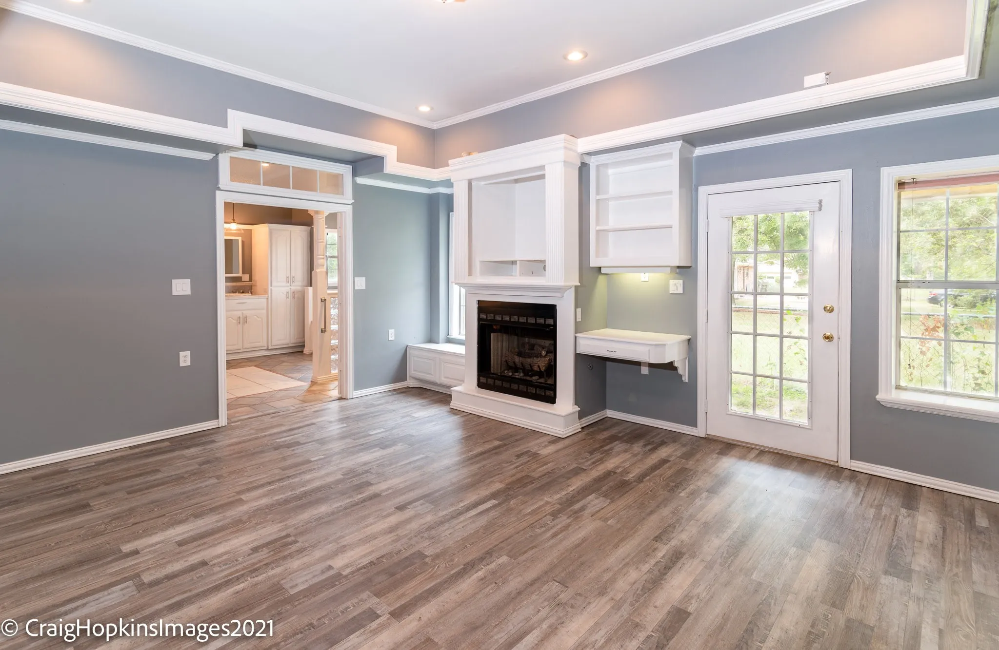 Living area featuring wood-finish flooring, a fireplace with built-in shelving, a glass-paneled door, and multiple windows