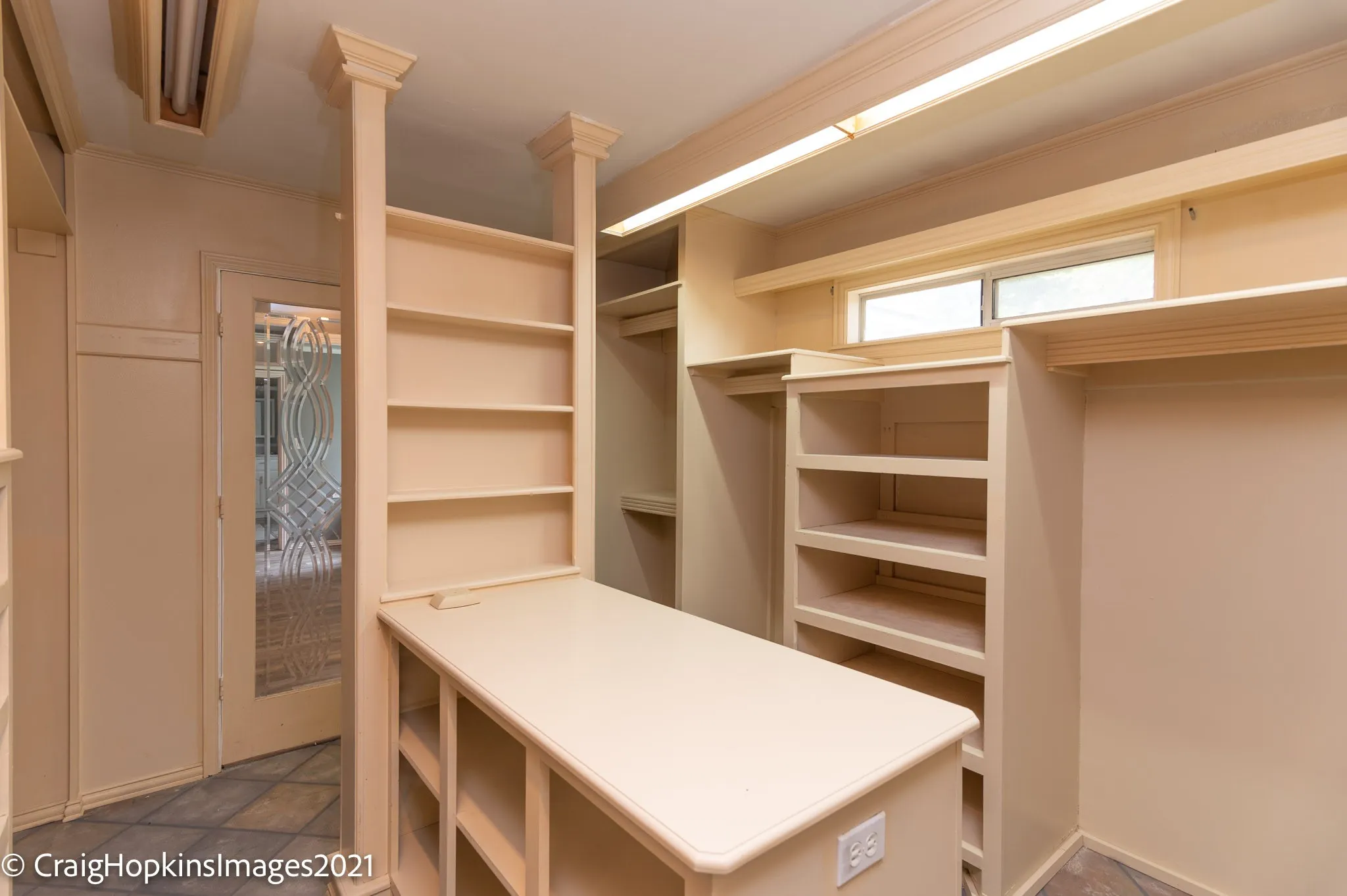 Custom closet system featuring a central island with integrated shelving, built-in open shelving, hanging rod space, and a decorative frosted glass door