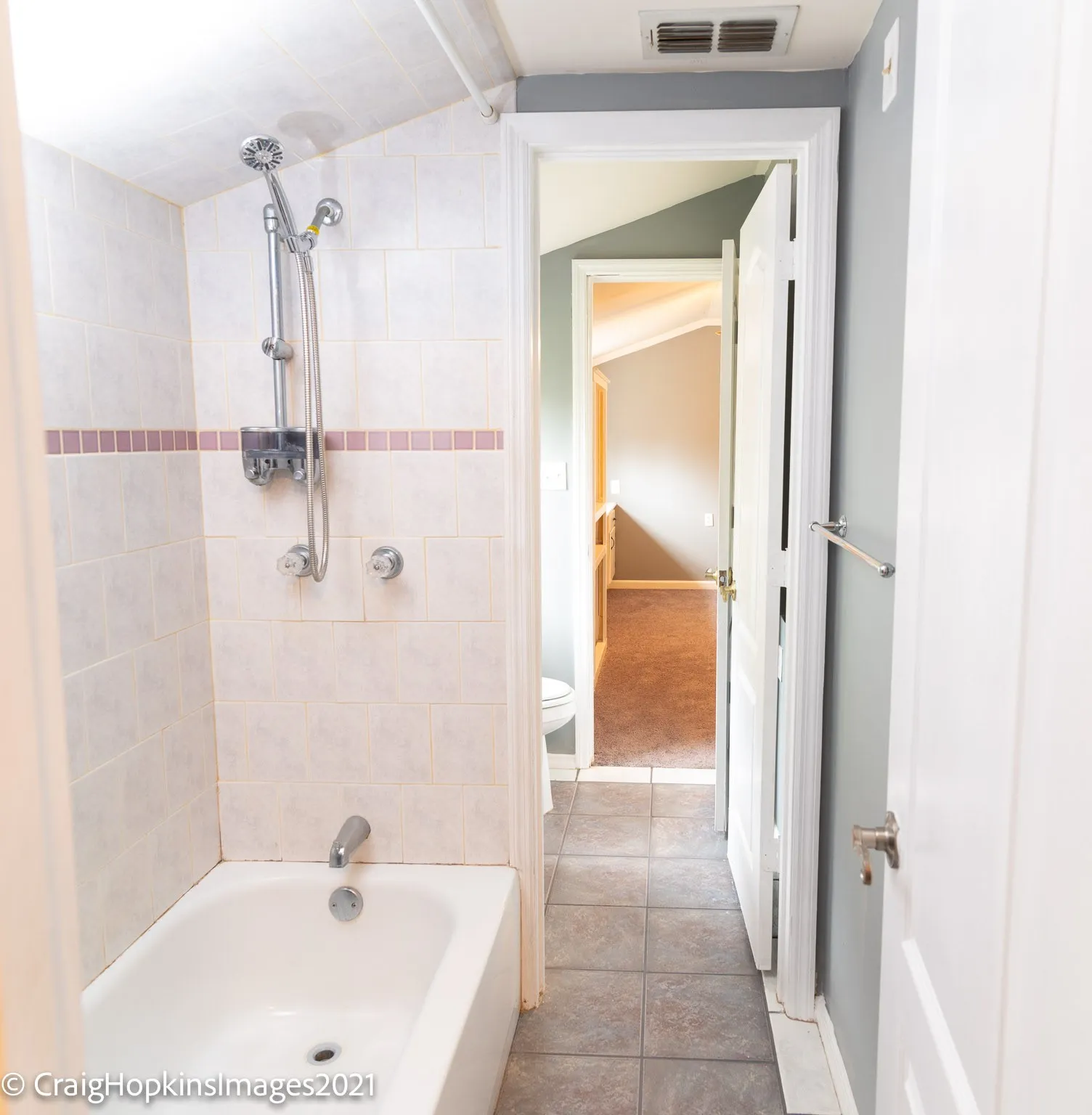 Bathroom with white subway tile shower surround, featuring a decorative pink tile accent band and an adjustable shower head