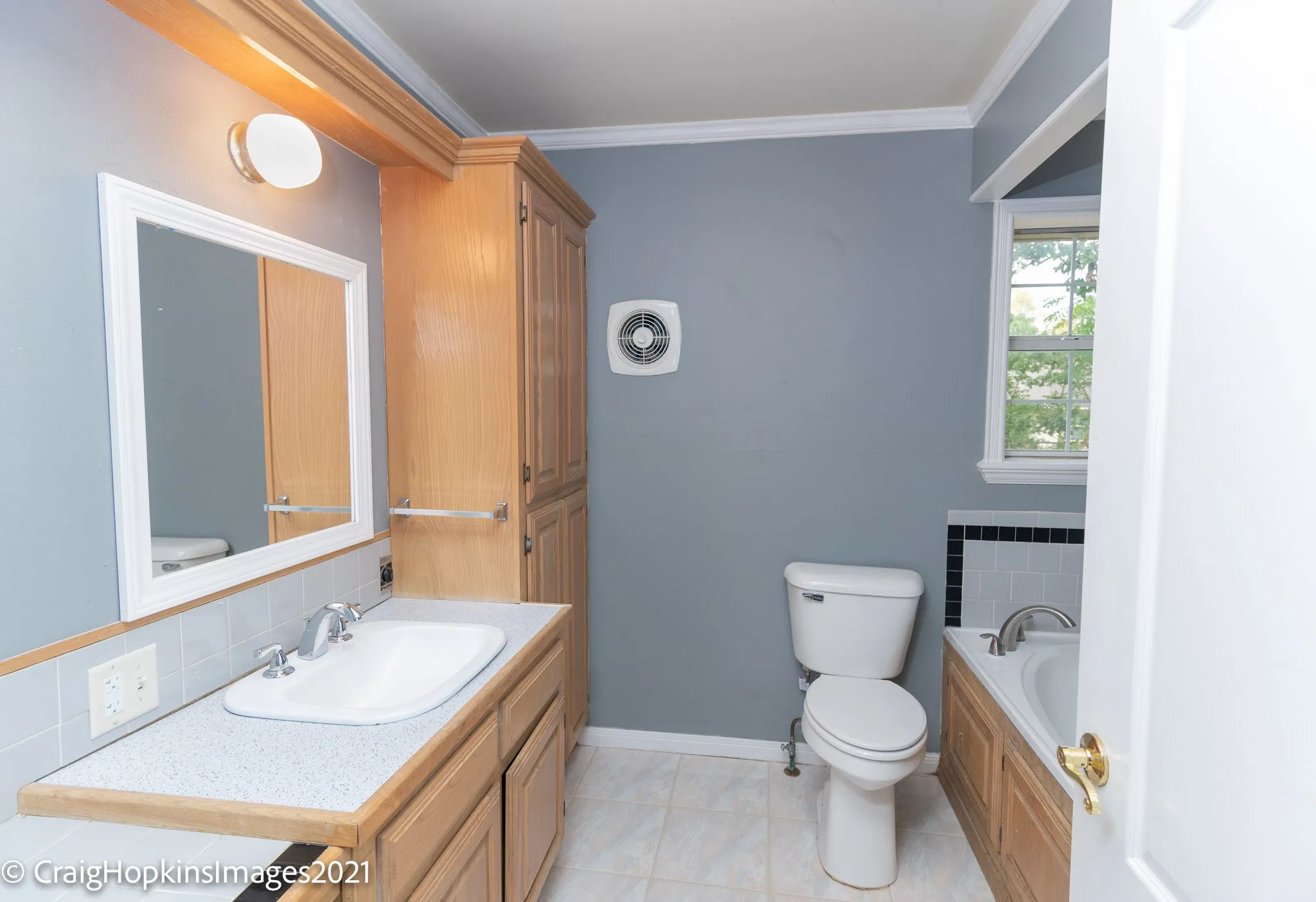 Bathroom featuring a single vanity with a white basin sink and chrome faucet, wood-finish cabinetry, a white framed mirror, and a built-in tub with tile surround