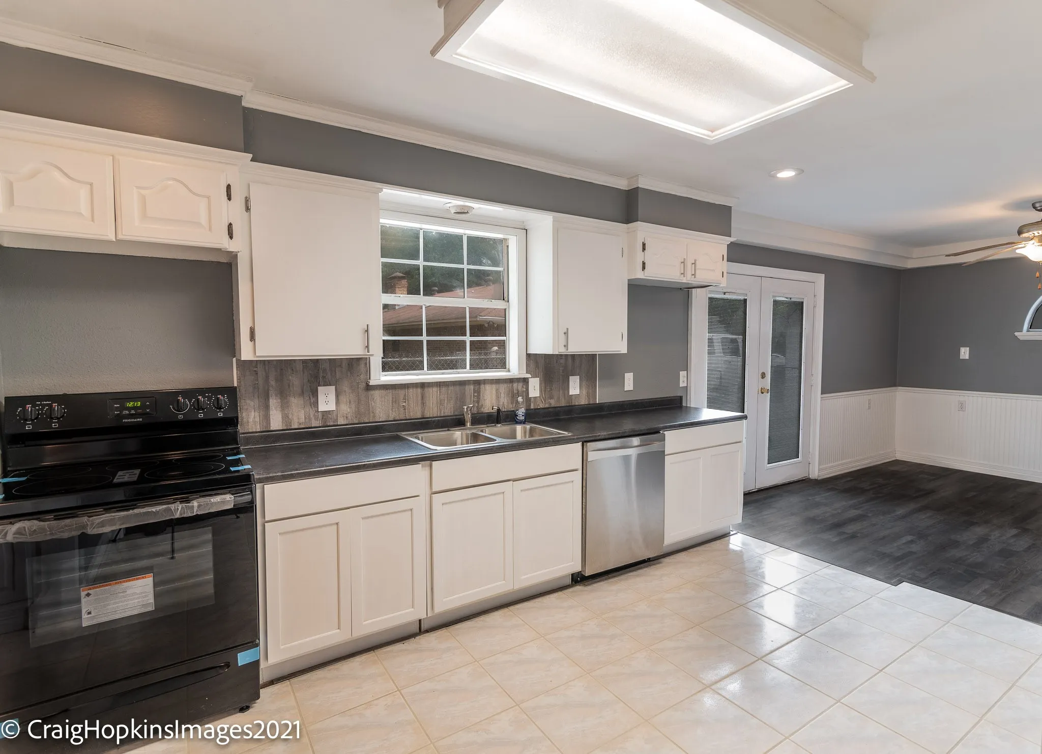 Kitchen featuring white cabinetry with dark countertops, a stainless steel double sink, and a black range