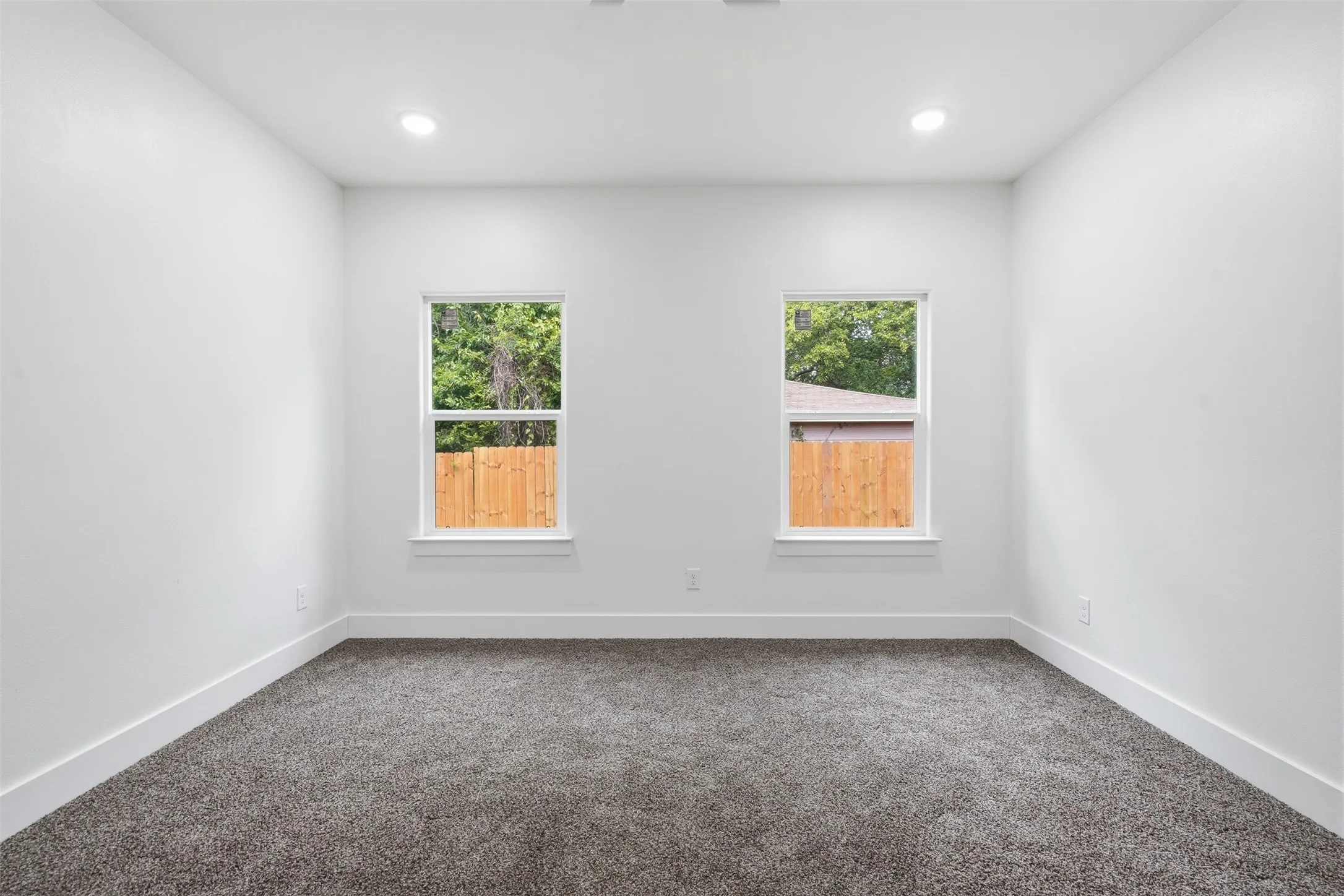 Room featuring two windows, neutral gray carpeting, white walls, white baseboards, and recessed lighting
