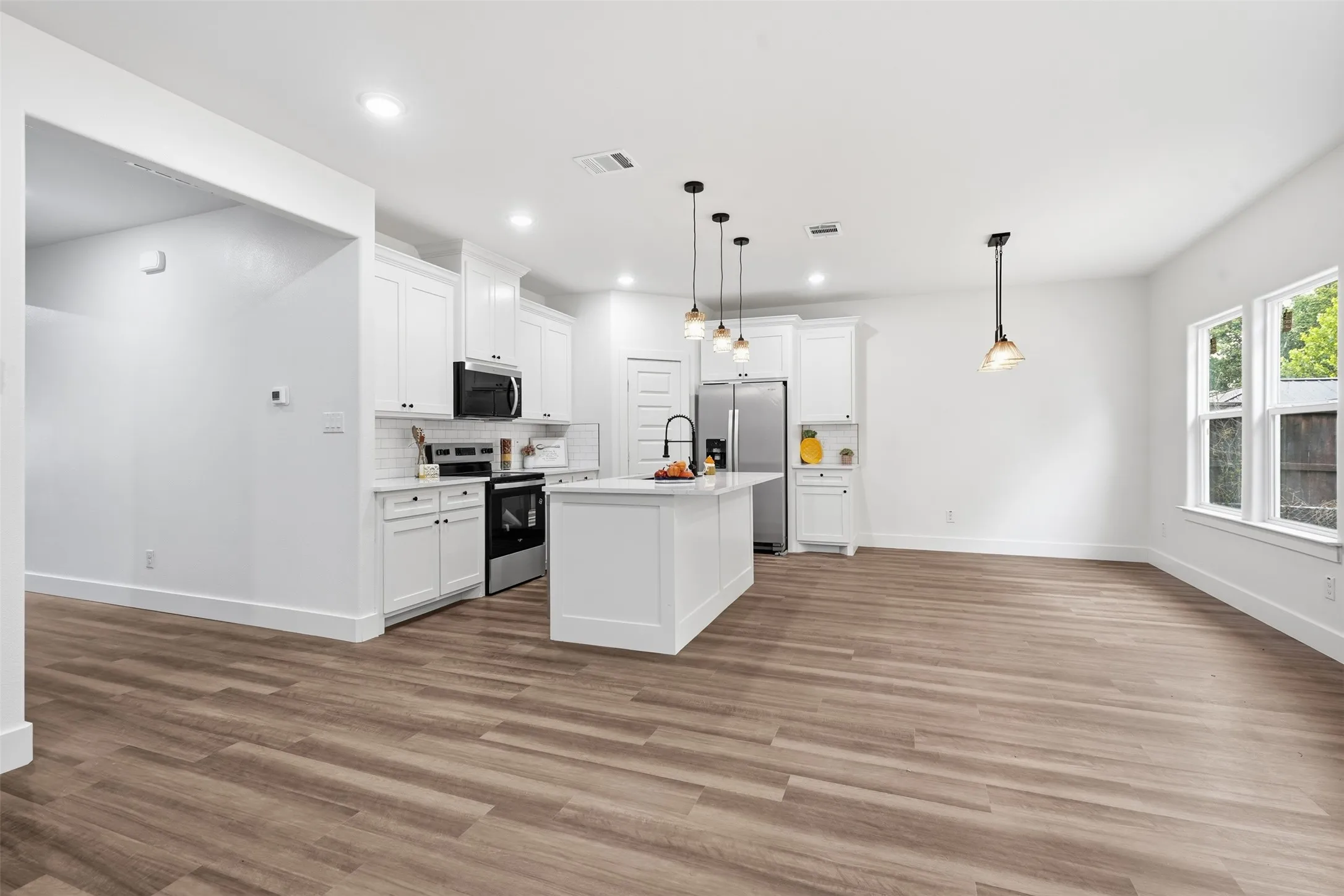 Modern open-concept kitchen featuring an island, white shaker cabinetry, stainless steel appliances, and wood-finish flooring