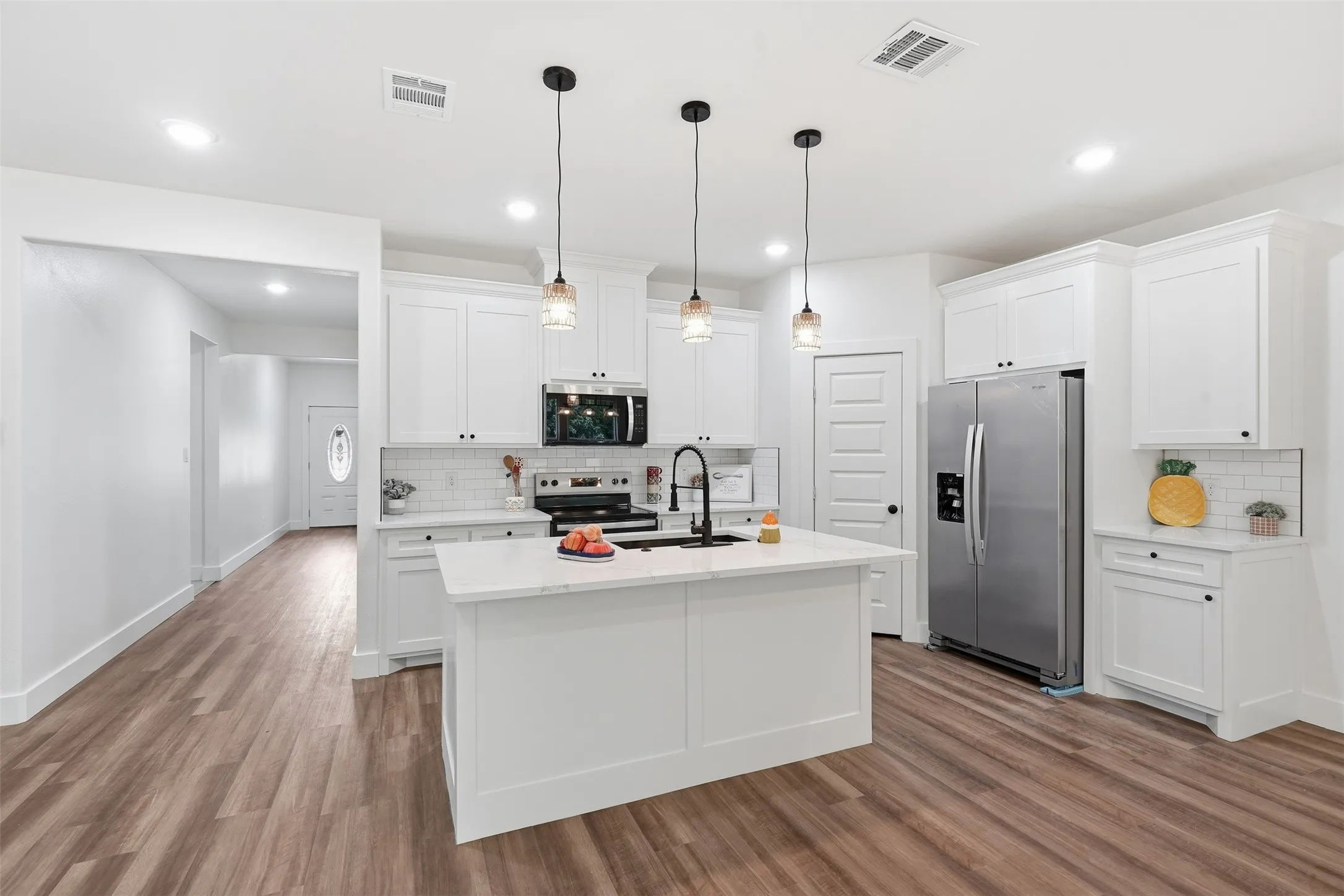 Modern kitchen featuring a central island with a solid surface countertop, white cabinetry with dark hardware, stainless steel appliances, recessed lighting, and wood-finish flooring