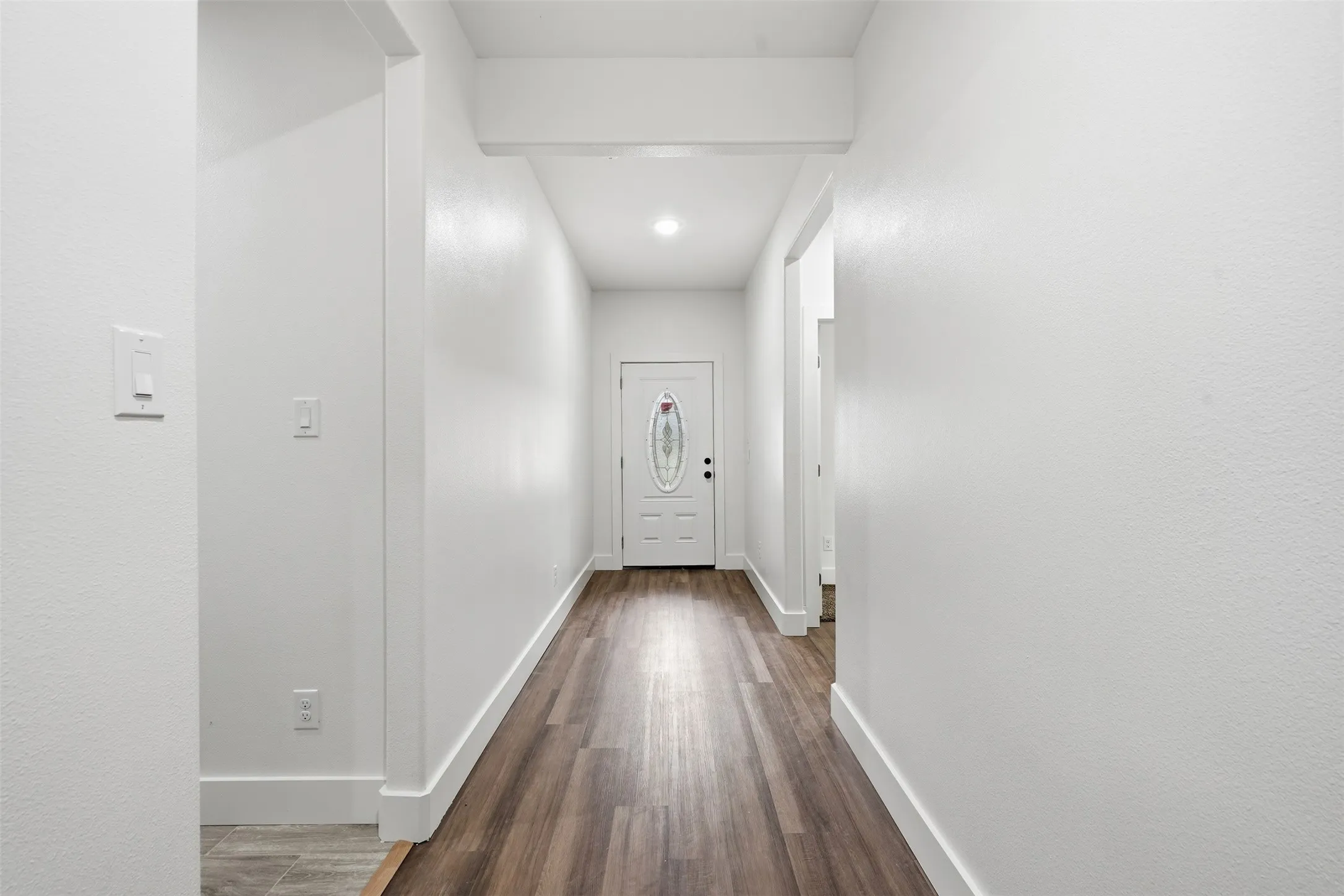 Hallway featuring wood-finish flooring, recessed lighting, and a white entry door with decorative glass
