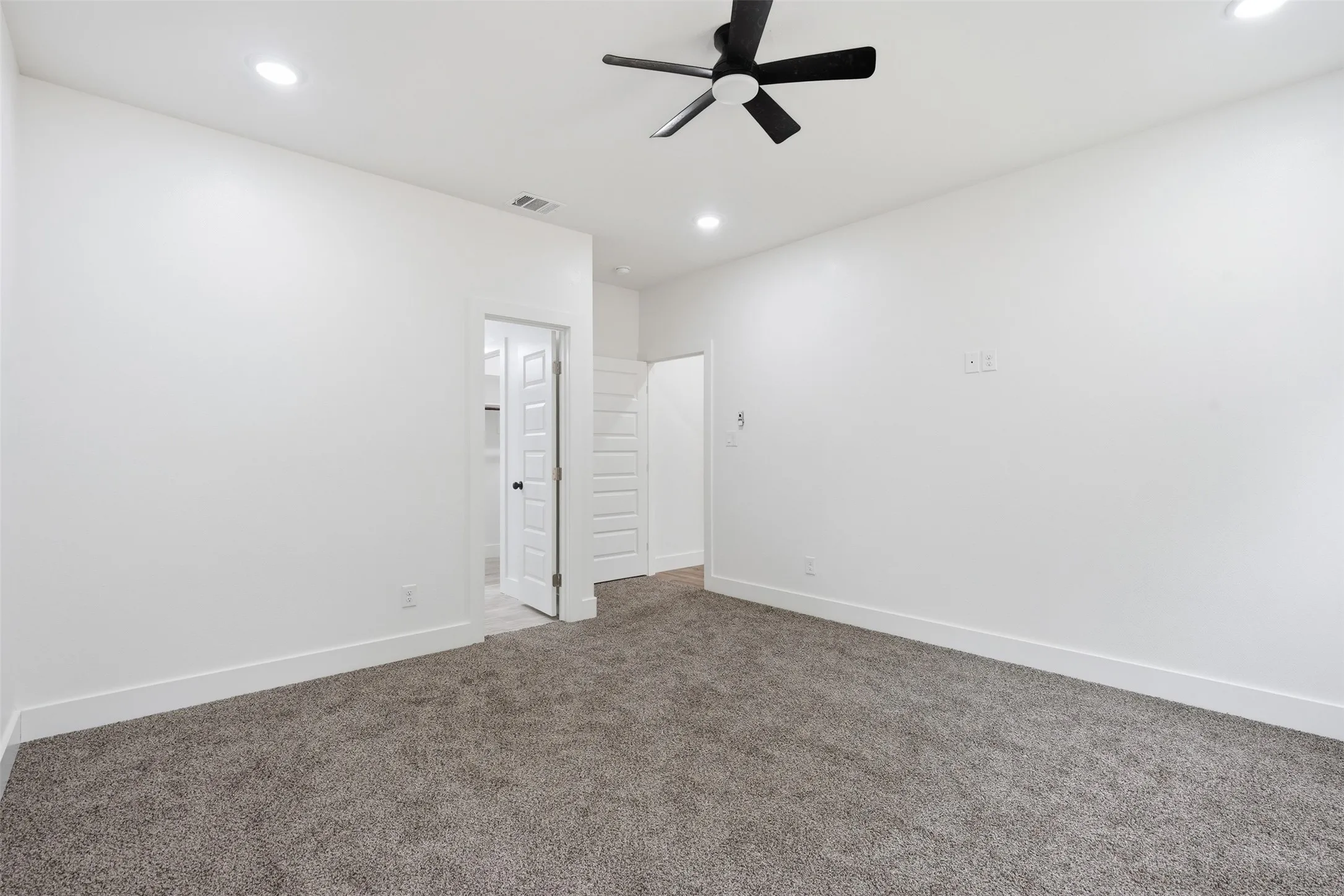 Spacious room featuring neutral carpeting, white walls, recessed lighting, and a modern black ceiling fan