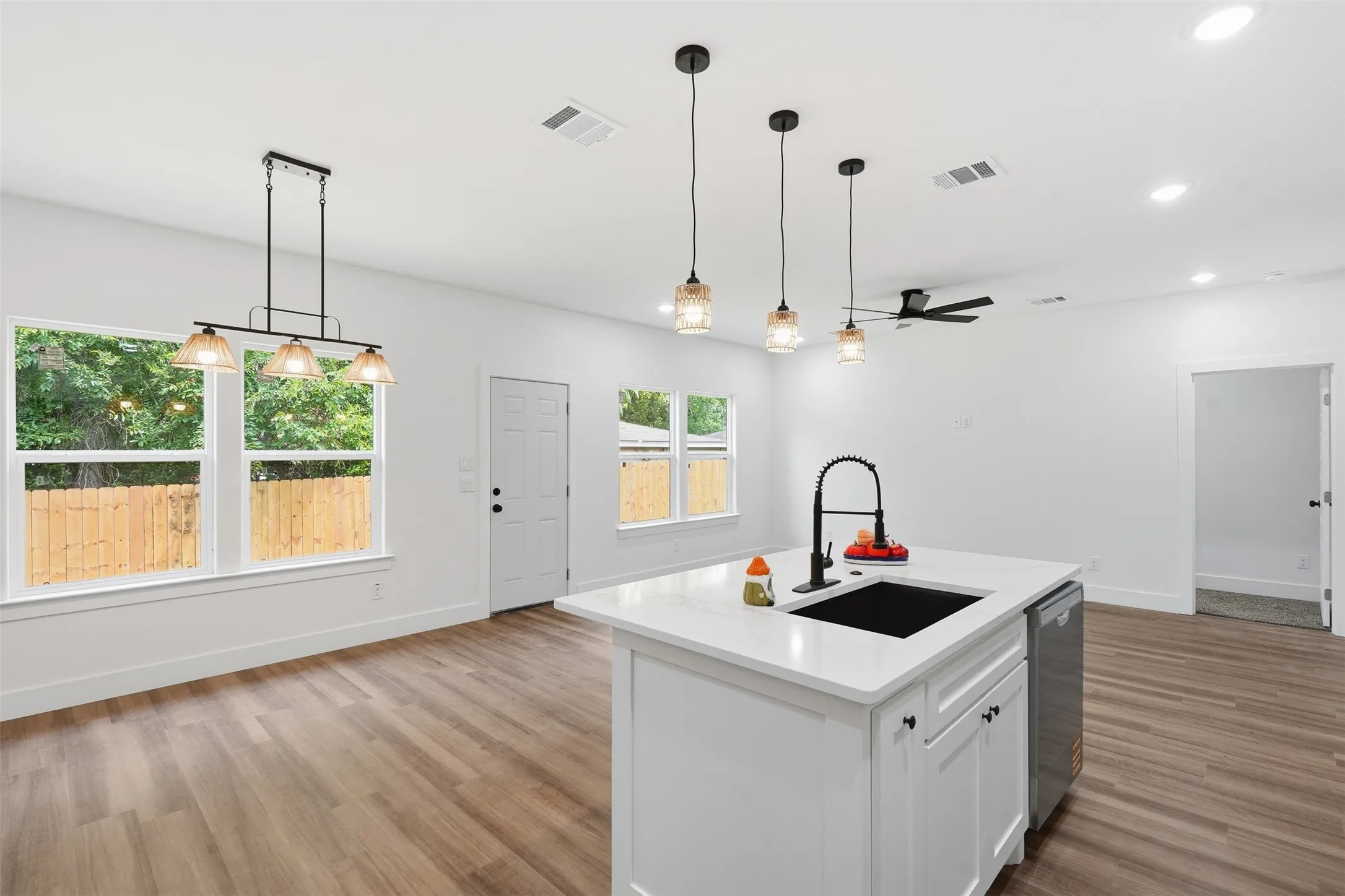 Open-concept interior featuring wood-finish flooring, white walls, and a contemporary kitchen island with a black sink and matte black faucet
