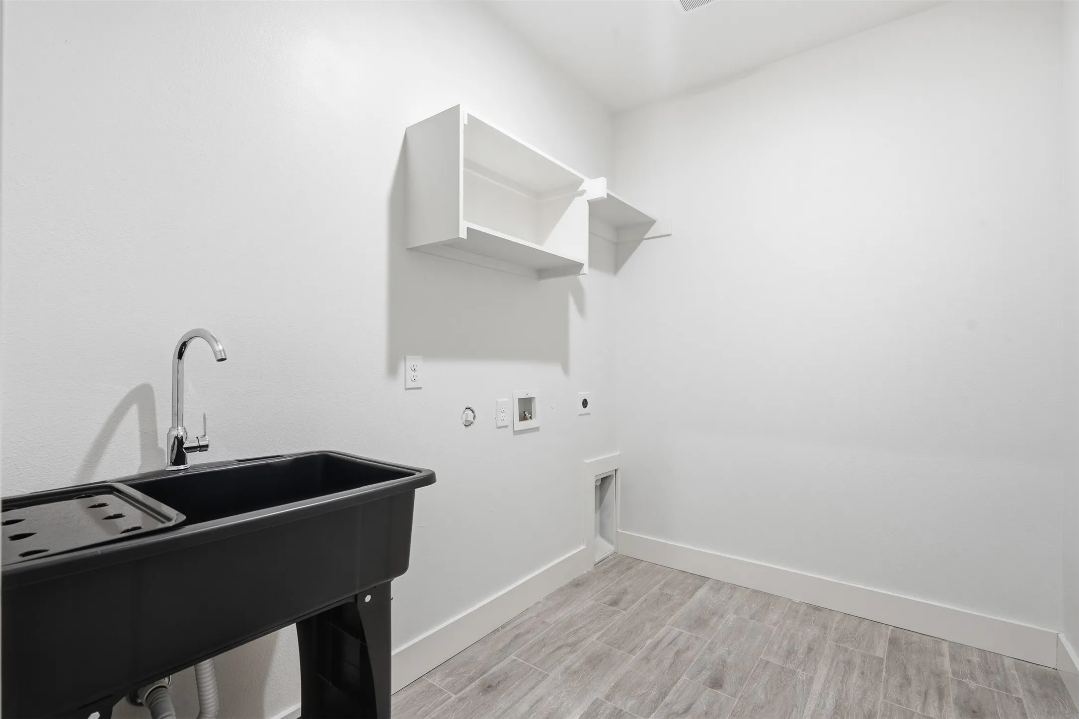 Laundry area featuring a utility sink with a chrome faucet, wood-finish flooring, white walls, and built-in shelving