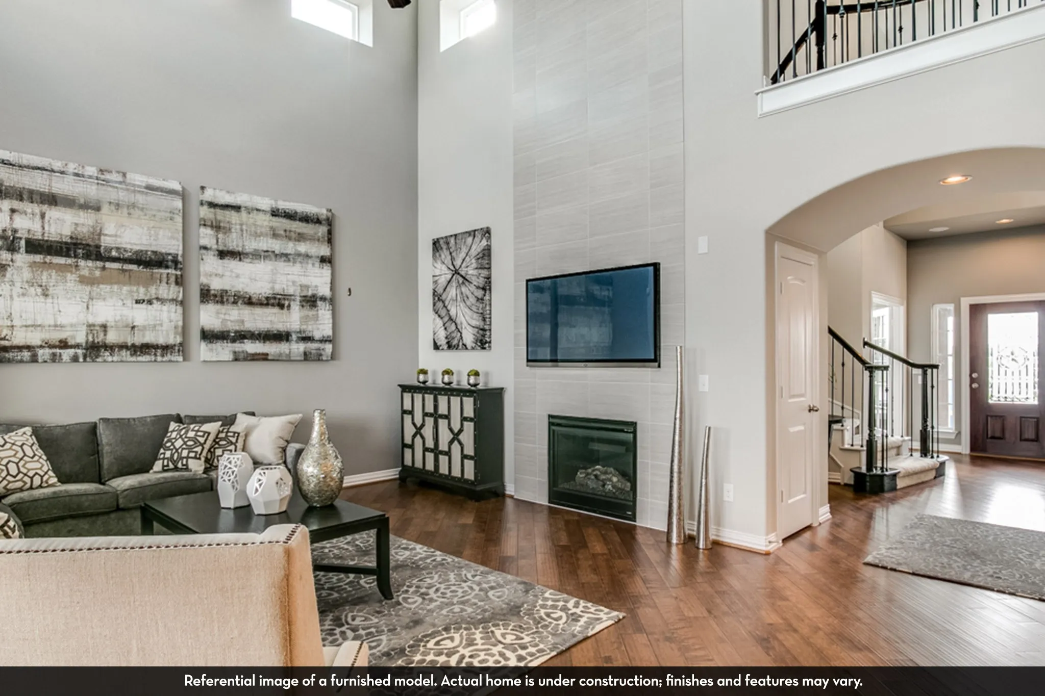 Two-story living area featuring wood-finish flooring, a contemporary fireplace with a light-toned tile surround, and an open-concept design