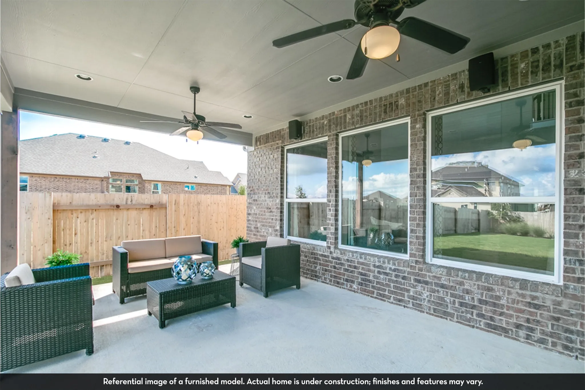 Covered outdoor patio featuring a concrete surface, a brick exterior wall with multiple windows, and two ceiling fans with integrated lighting