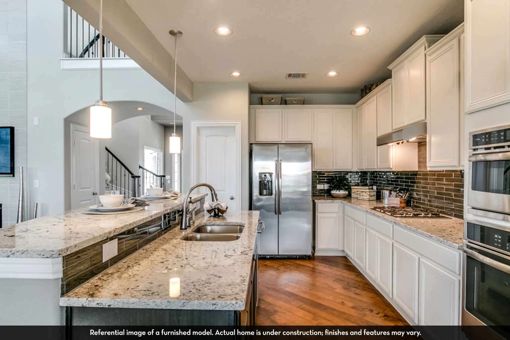 Open-concept kitchen featuring an expansive island with a double sink, white cabinetry, integrated stainless steel appliances, and wood-finish flooring
