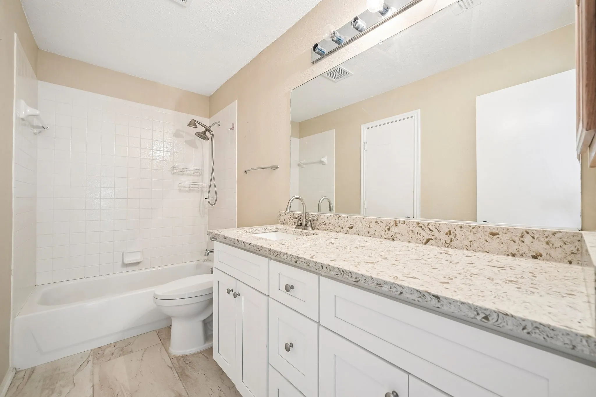 Bathroom featuring a spacious vanity with a light-toned countertop, white cabinetry with silver-tone hardware, and an integrated sink