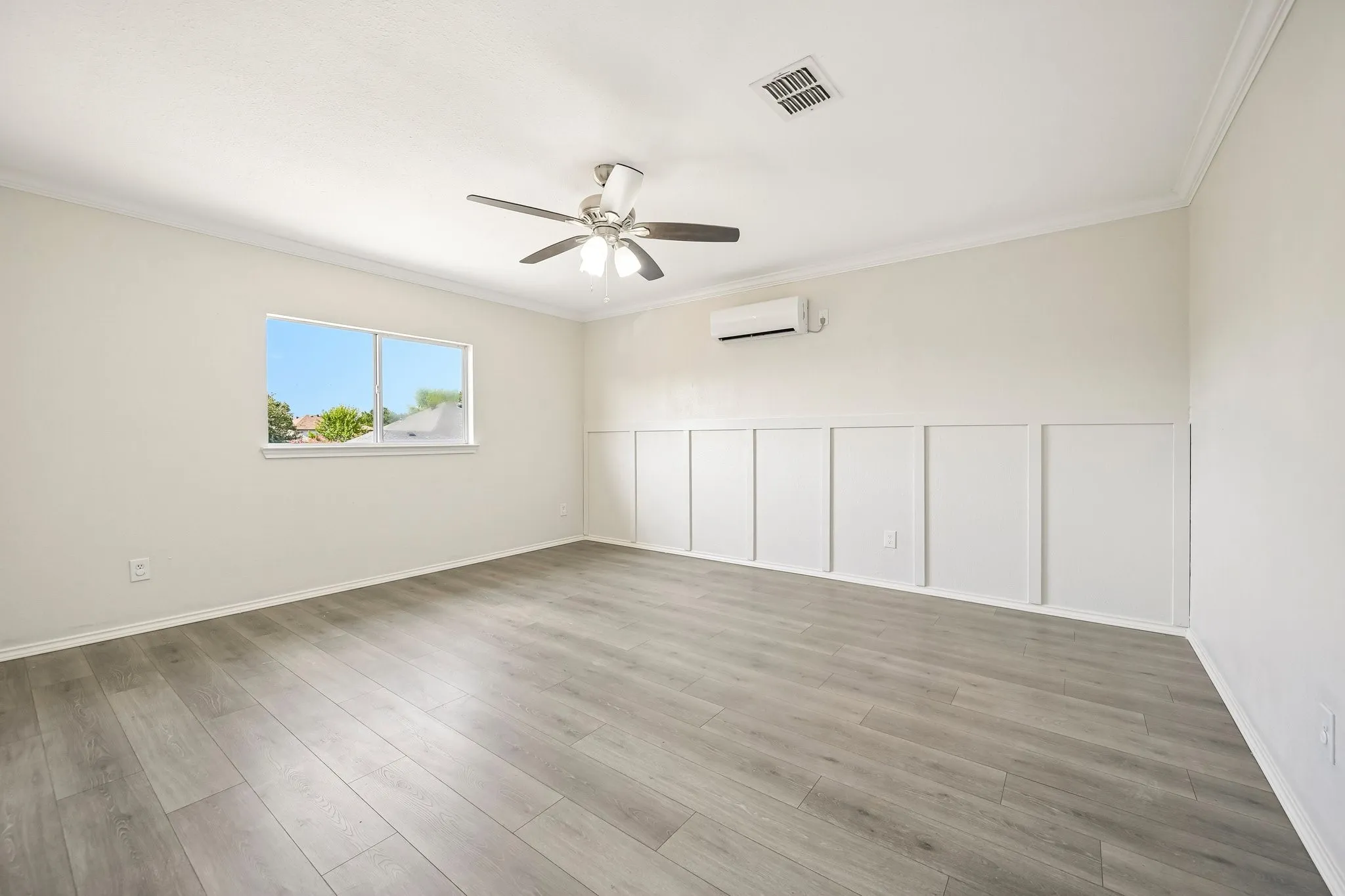 Spacious room featuring wood-finish flooring, a contemporary ceiling fan, and wall paneling