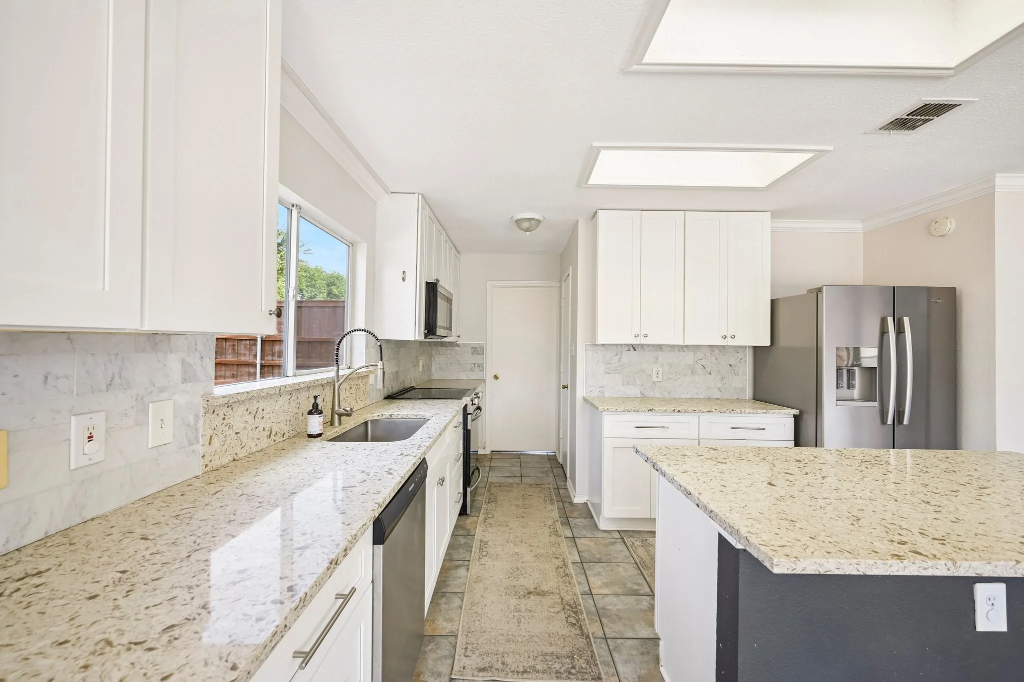 Bright kitchen featuring white cabinetry, light-toned countertops, a stainless steel sink, and recessed lighting