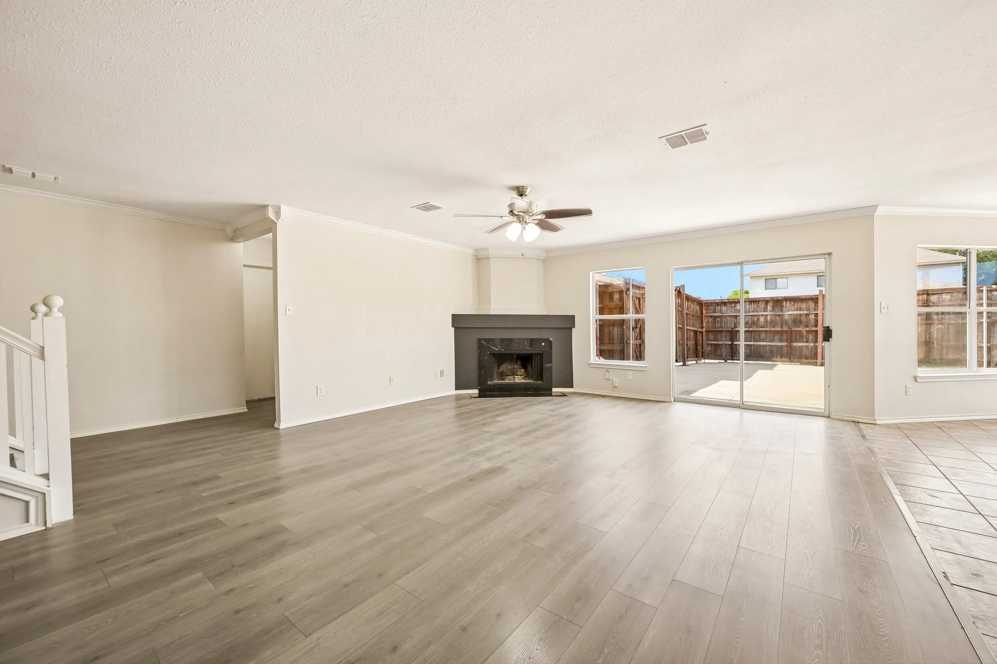 Spacious living area featuring light wood-finish flooring, a dark-toned fireplace, and a ceiling fan