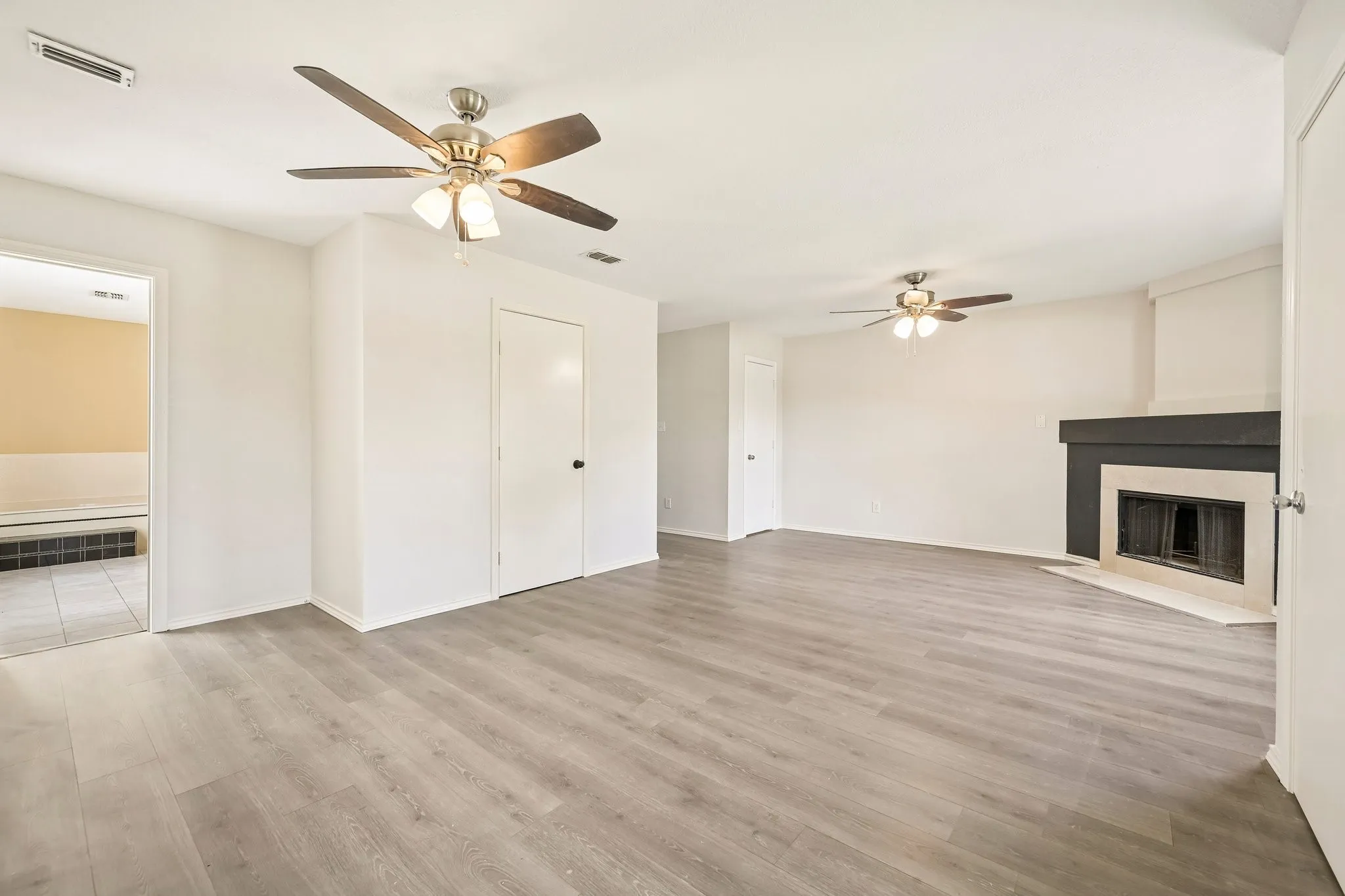Spacious room featuring wood-finish flooring, a contemporary fireplace with dark mantel, and dual ceiling fans with integrated lighting