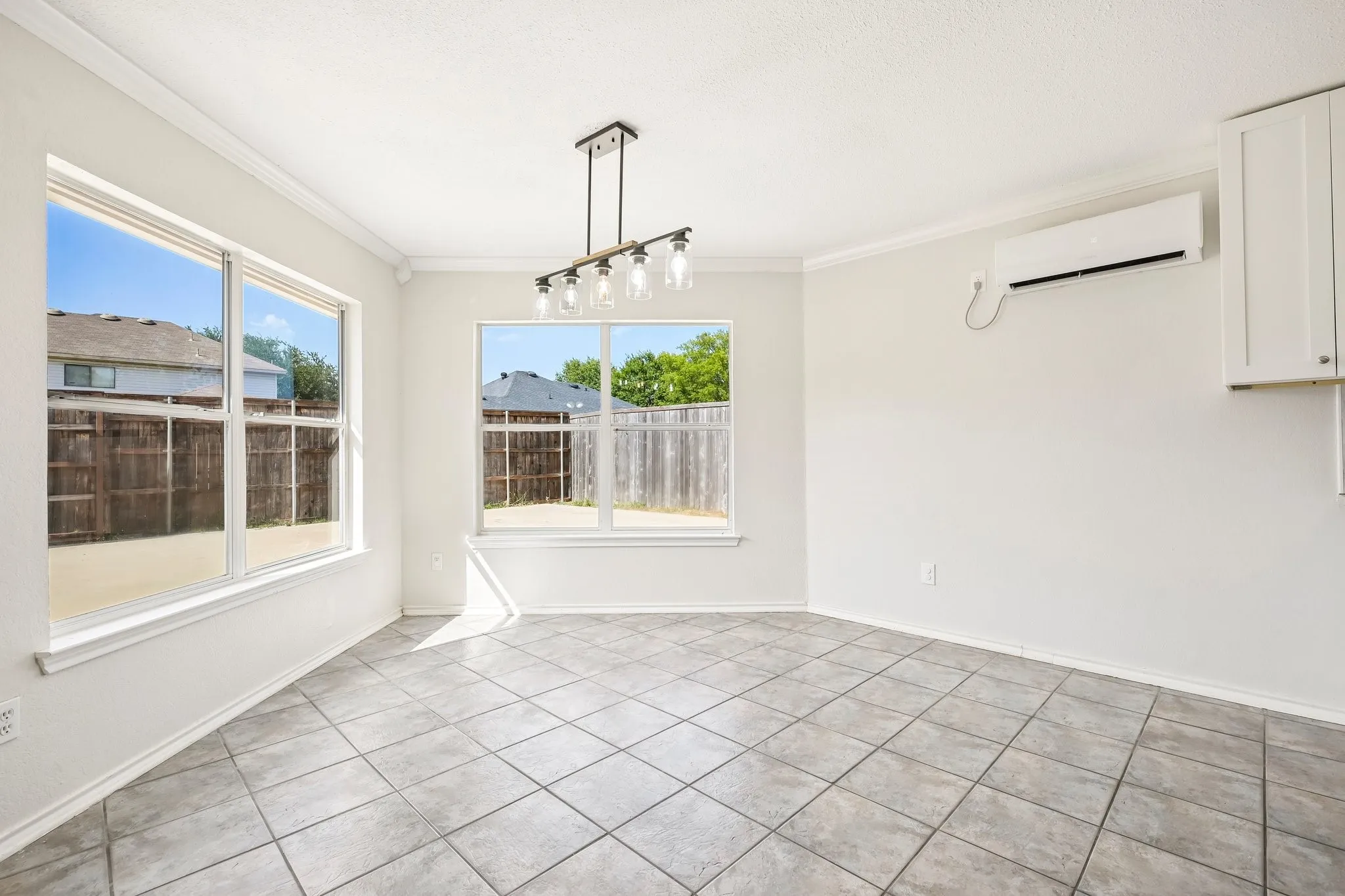 Bright interior space featuring large windows, neutral wall tones, square tile flooring, a linear chandelier, and an integrated wall-mounted HVAC unit