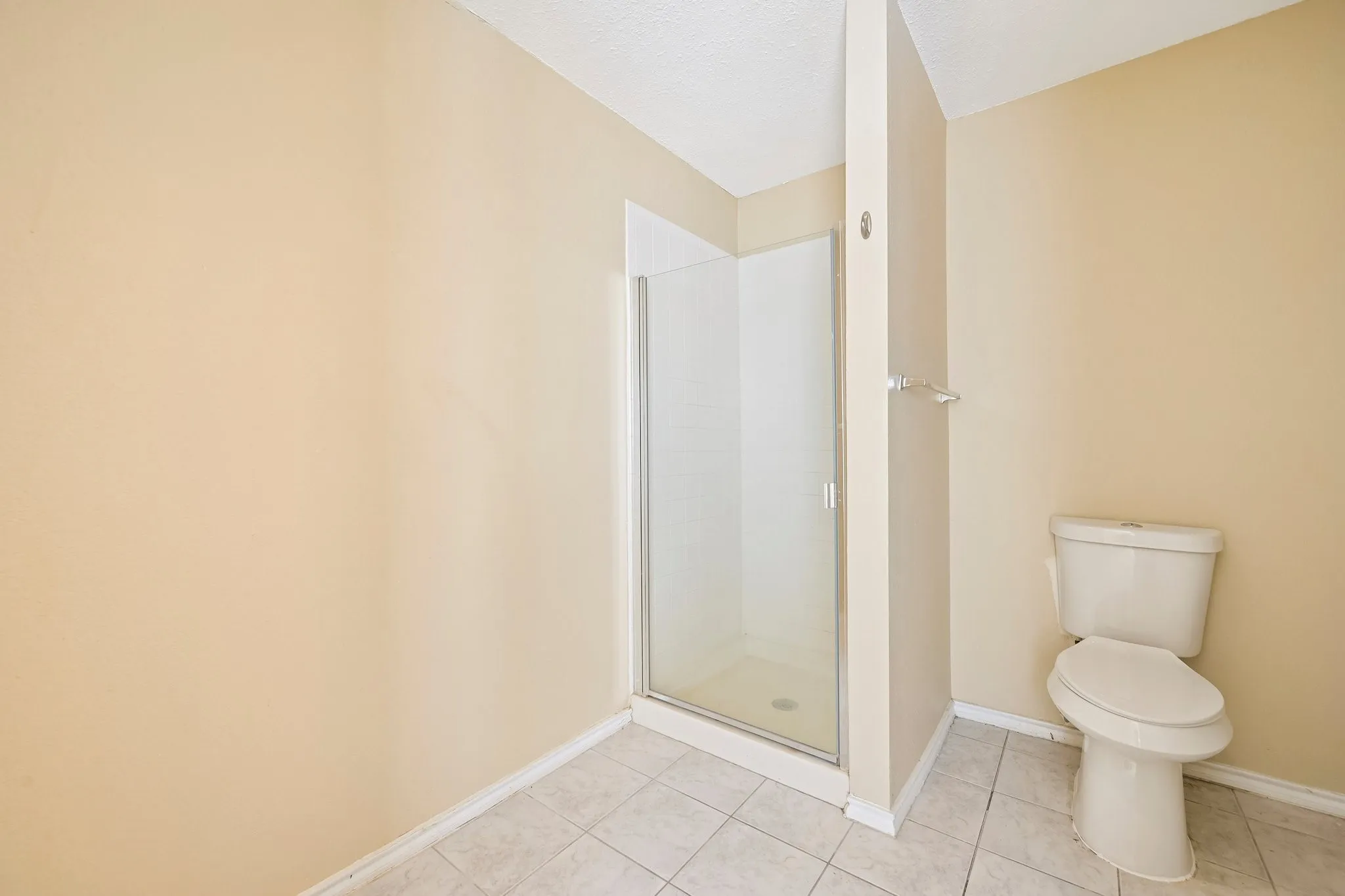 Spacious bathroom featuring a glass-enclosed shower, white ceramic tile flooring, and a white toilet