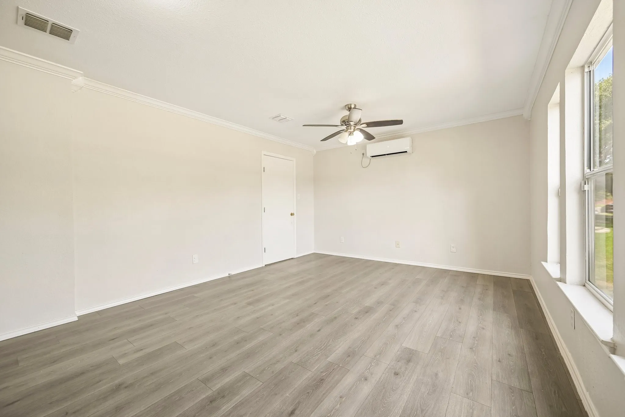 Spacious room featuring wood-finish flooring, white walls, and crown molding