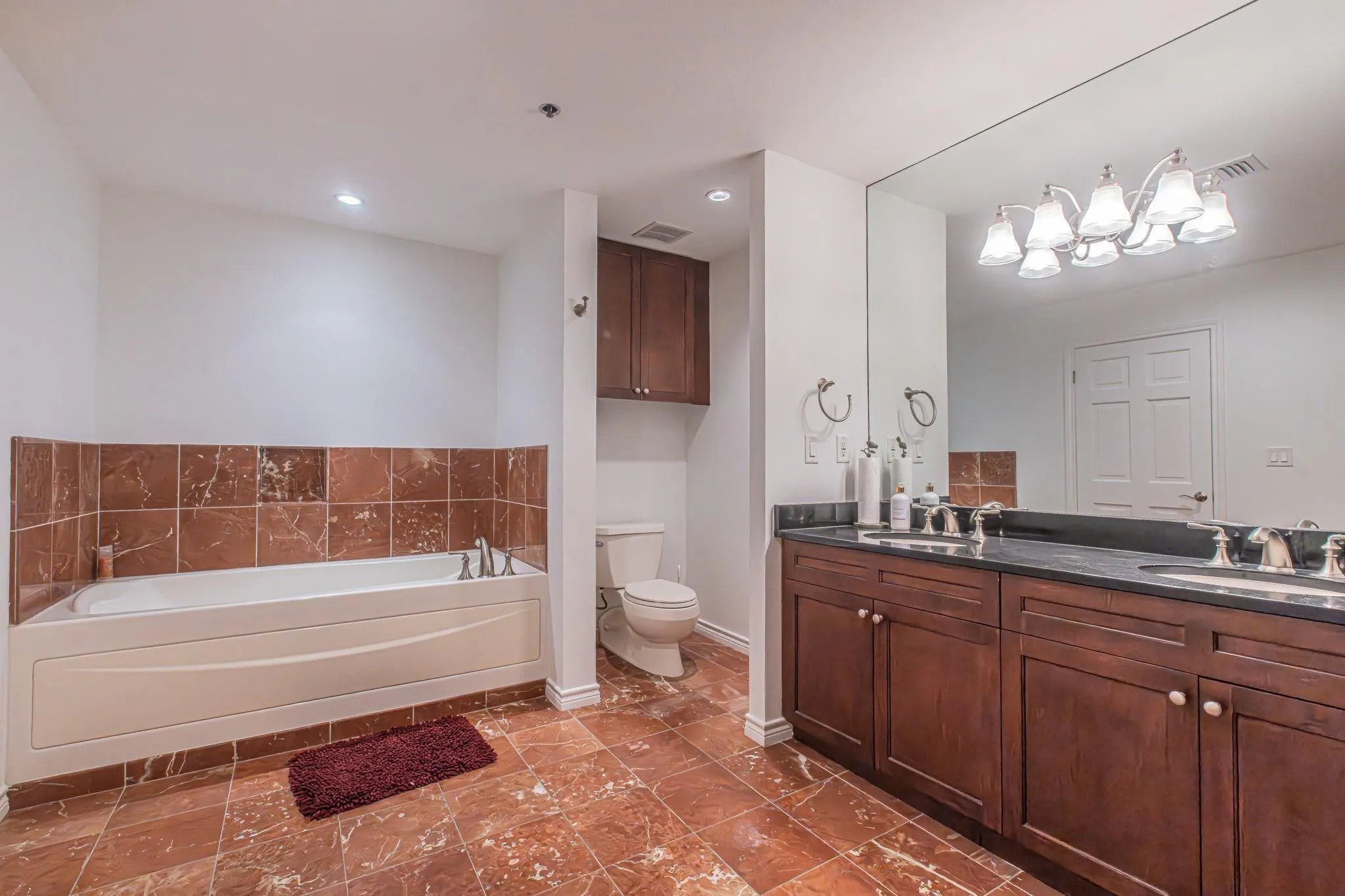 Bathroom featuring a built-in tub with tile surround, a dark wood-finish double vanity with dual undermount sinks and dark countertop, and a large wall-mounted mirror