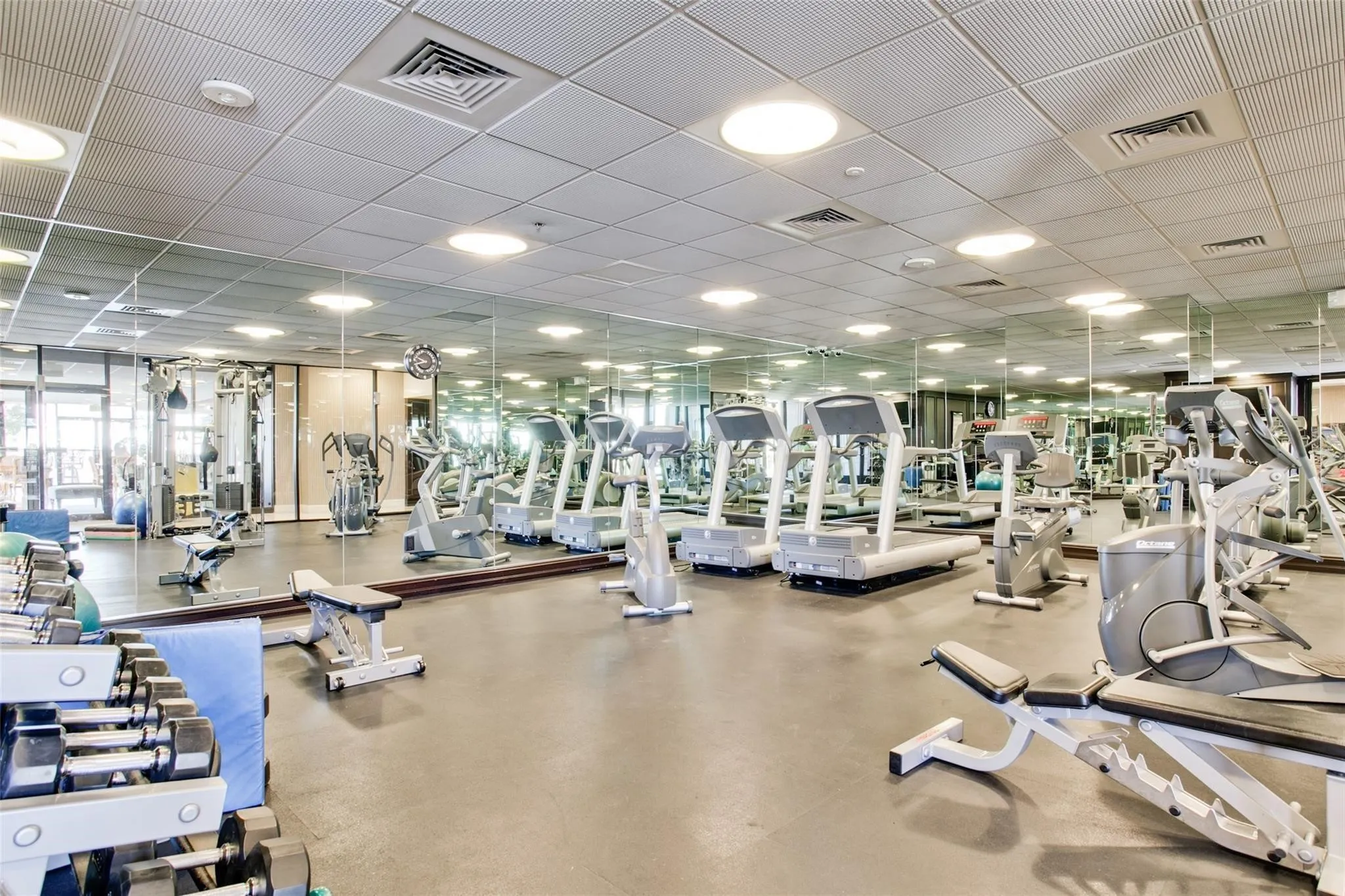 Spacious fitness center featuring a variety of cardio equipment, strength training machines, free weights, full-wall mirrors, and recessed ceiling lighting