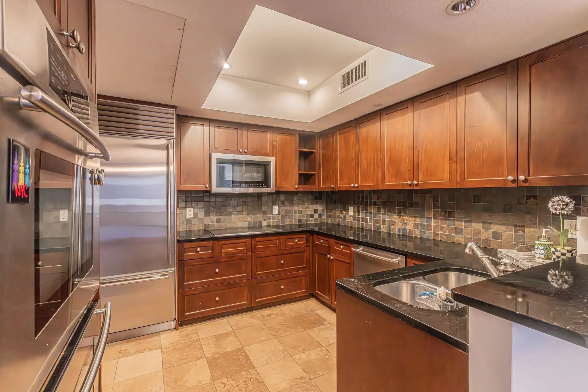 Gourmet kitchen featuring stainless steel appliances, dark wood cabinetry, a tiled backsplash, granite countertops, and light-toned tile flooring