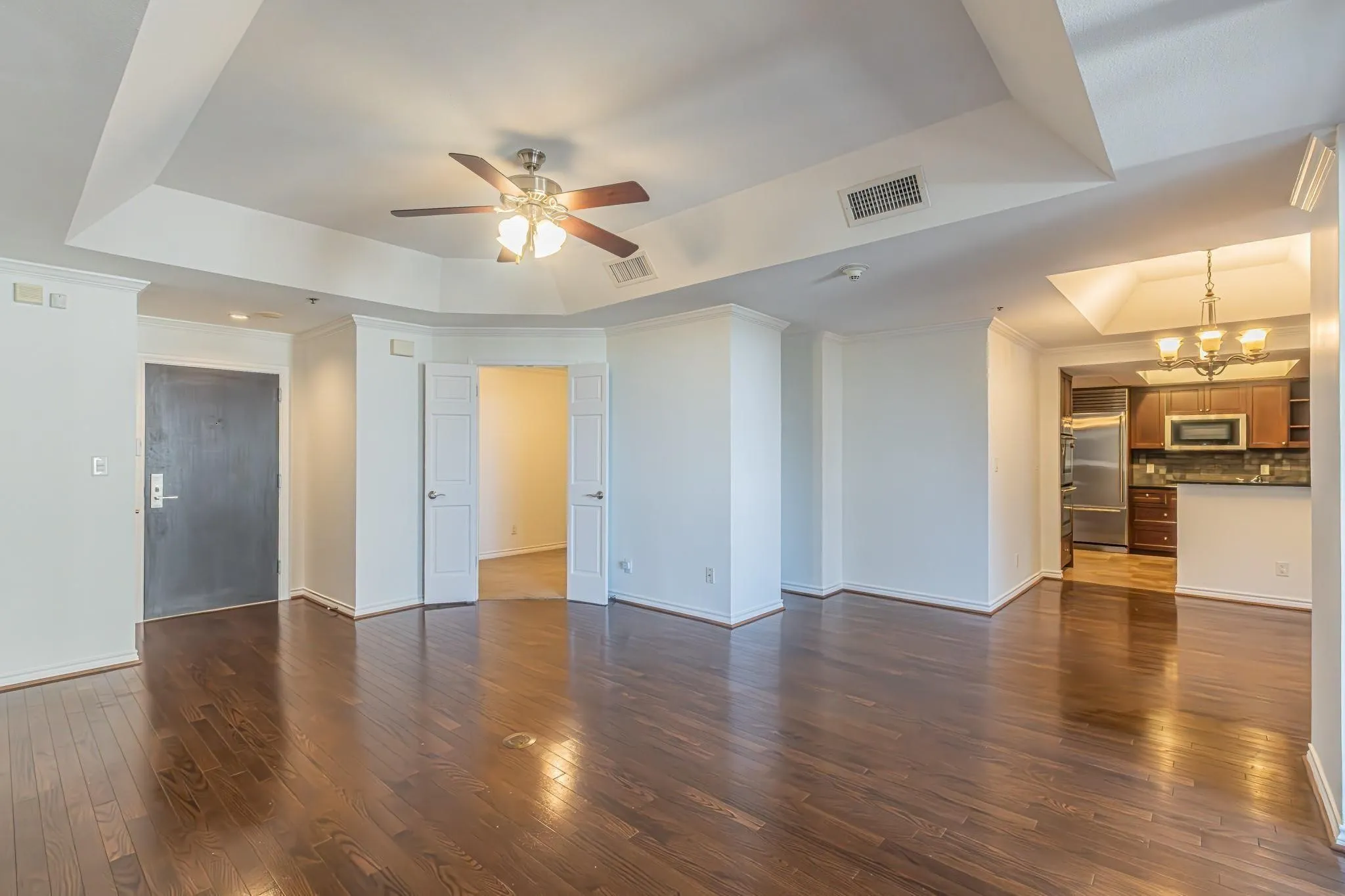 Spacious open-concept living area featuring rich wood-finish flooring, a tray ceiling with a ceiling fan, and white baseboards