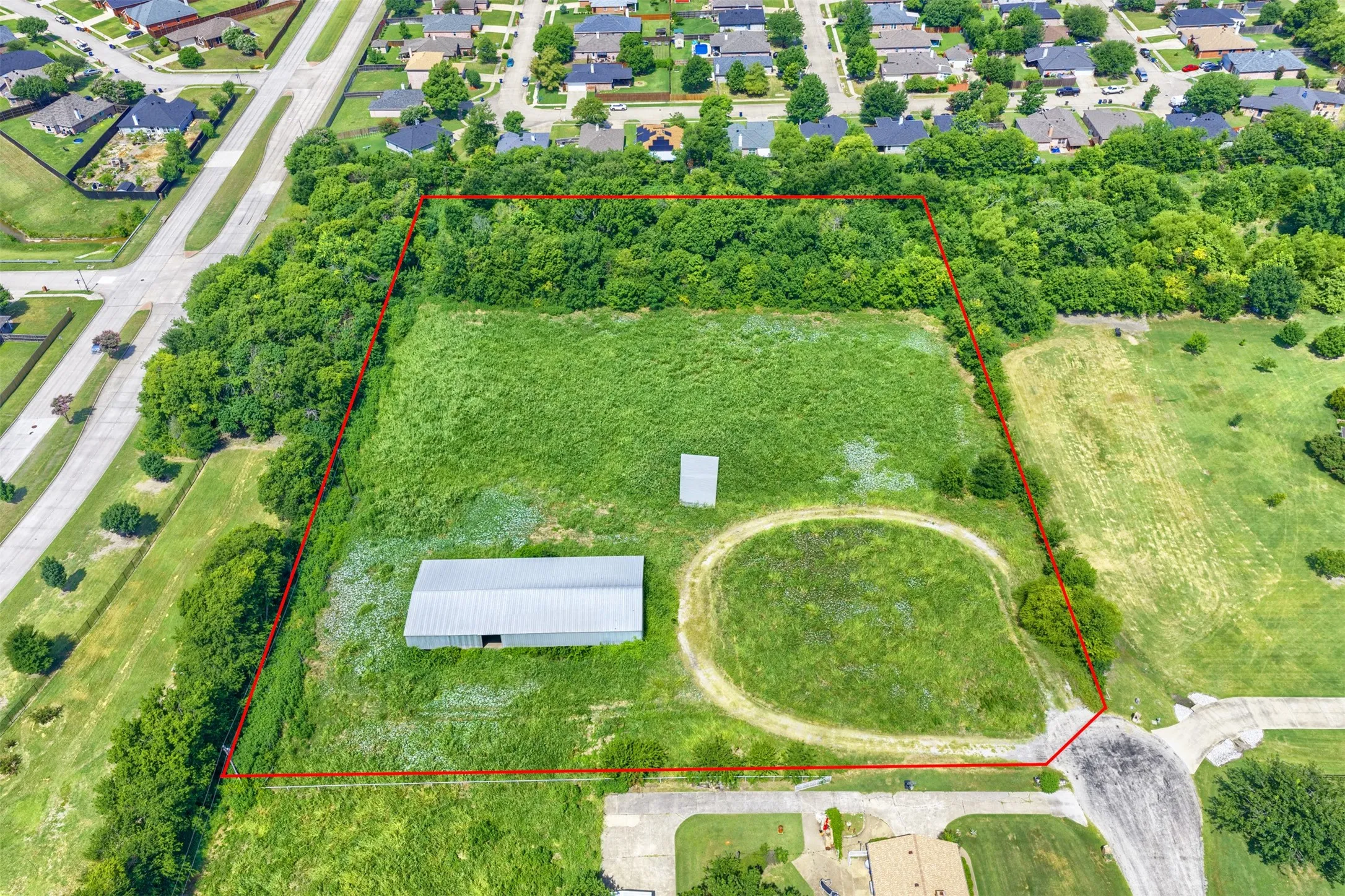 Expansive land parcel featuring open green space, a large metal outbuilding, and a smaller ancillary structure