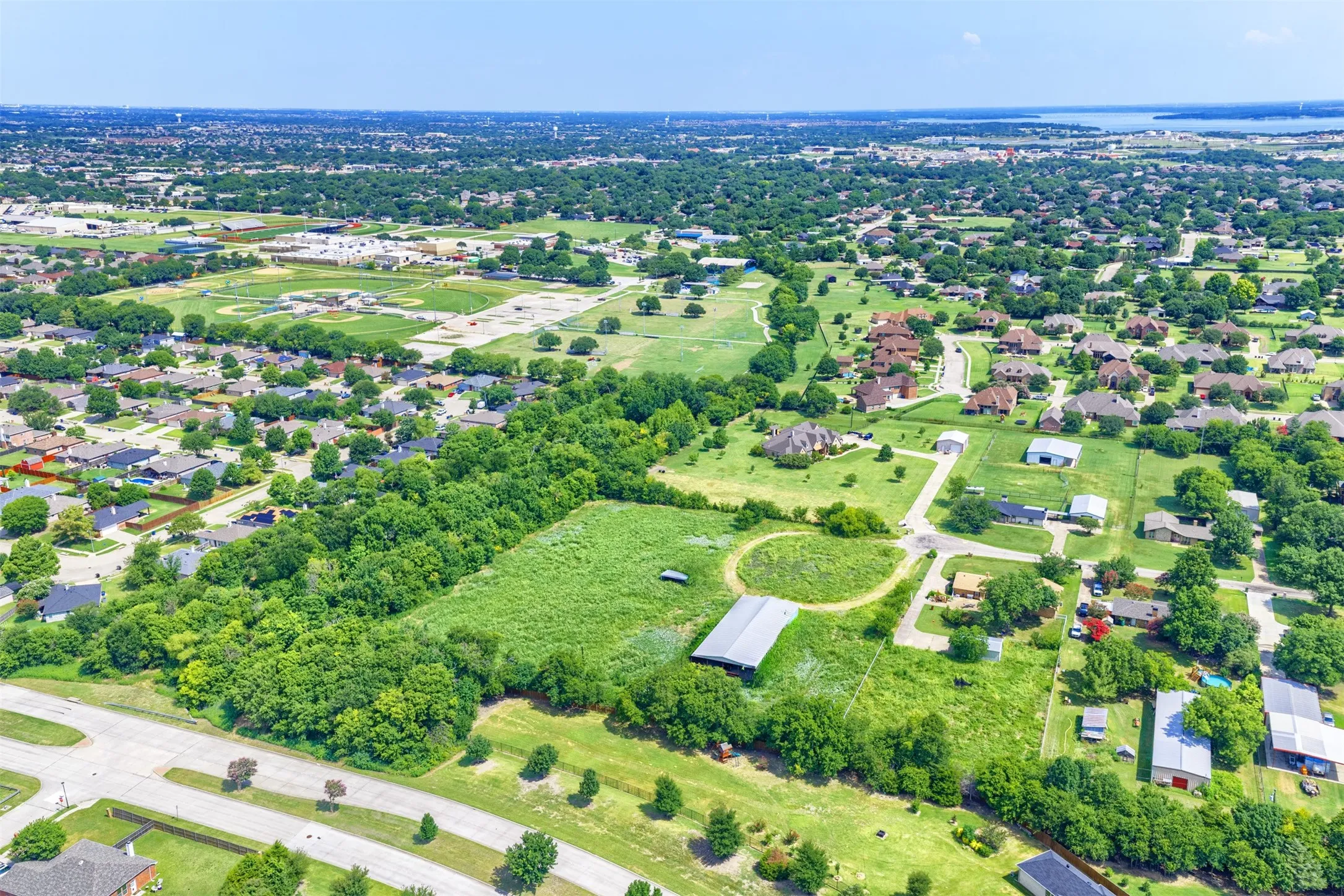 Expansive land parcel featuring open fields, mature tree lines, and a large metal barn structure