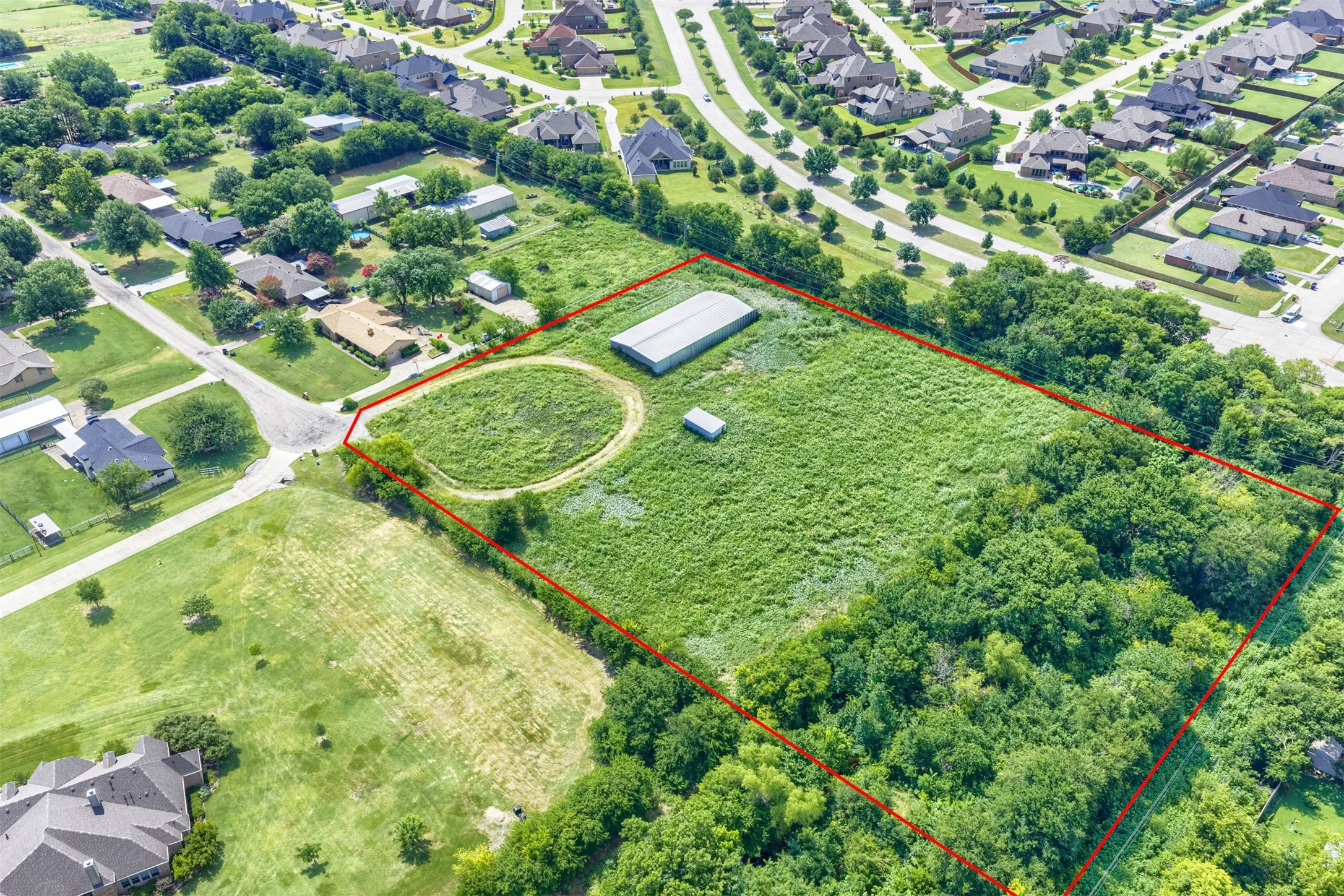 Expansive land parcel featuring open grassy areas, mature trees, a large metal barn, and a smaller outbuilding