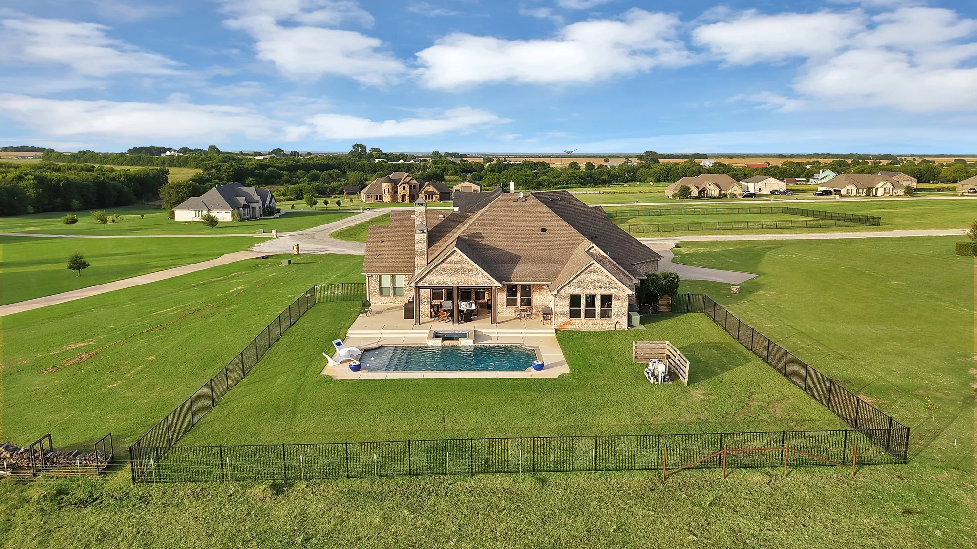 Rear exterior featuring a rectangular in-ground swimming pool, an expansive patio area, and a large fenced lawn