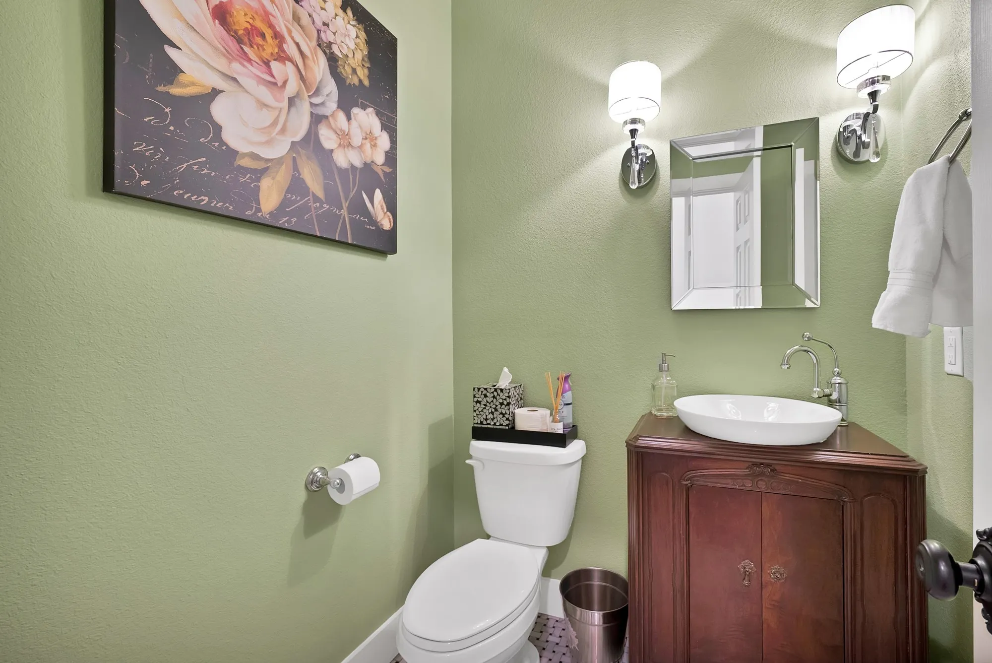 Powder room featuring a corner vanity with a vessel sink, dual wall sconces, a framed mirror, and hexagonal floor tiling