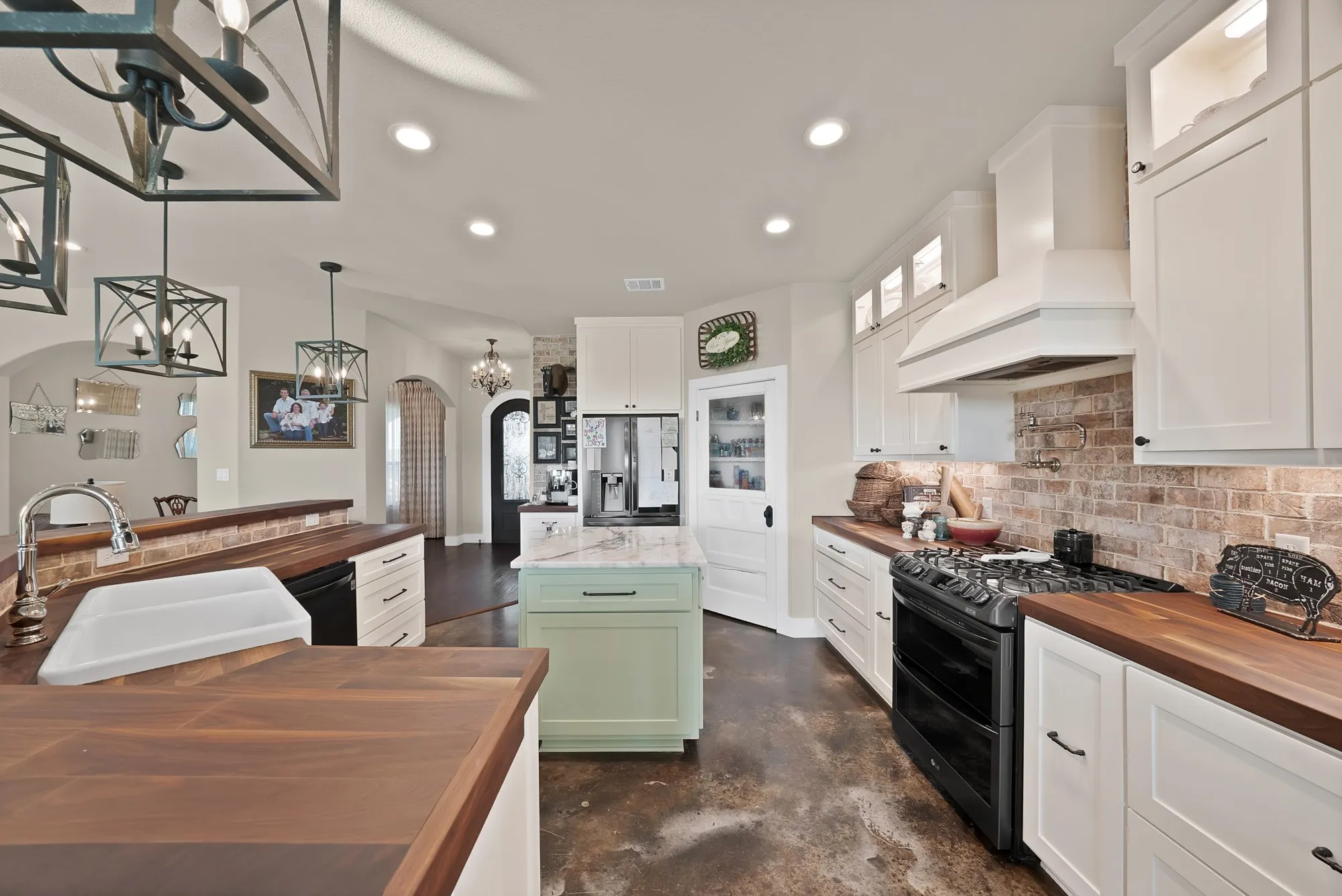 Kitchen featuring butcher block countertops, white cabinetry with display uppers, a light green center island, a full-size refrigerator, and a gas range with a brick backsplash