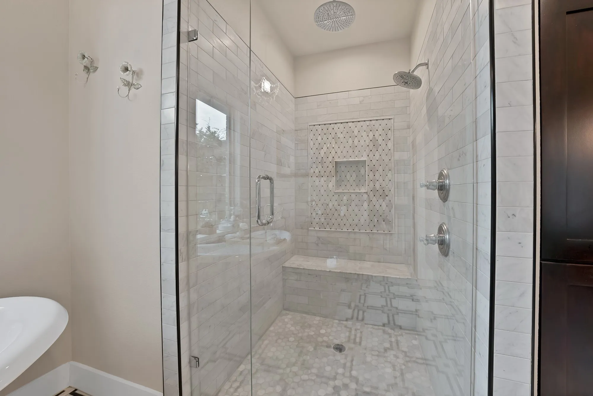 Glass-enclosed shower featuring white subway tile, a decorative mosaic tile accent wall, a built-in bench, and a dual shower head system including a rainfall shower
