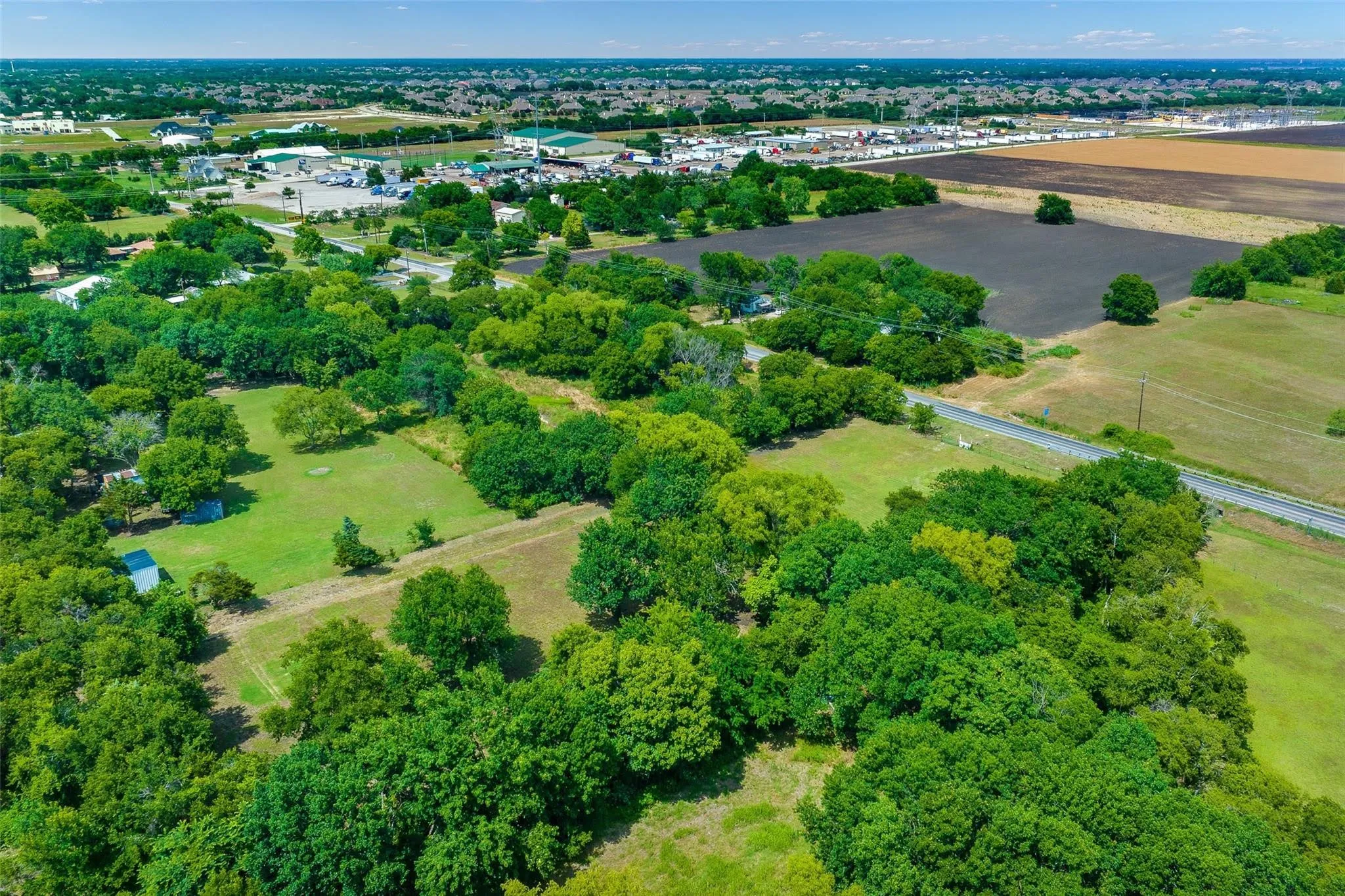 Expansive acreage featuring abundant mature trees, open grassy areas, and a visible road frontage