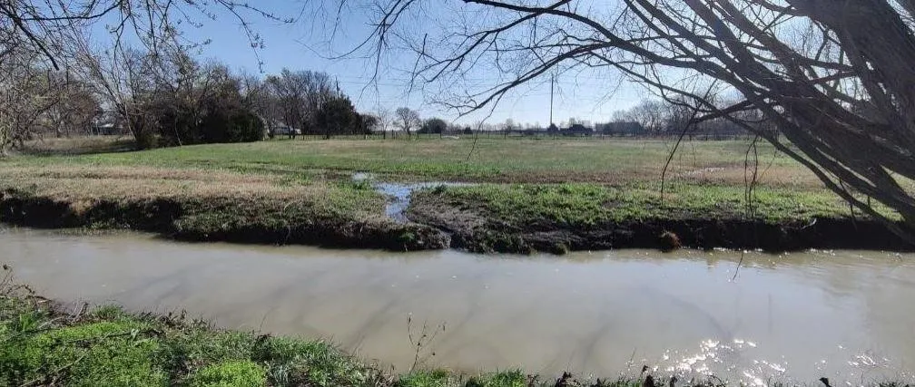 Natural waterway bordering an expansive grassy field