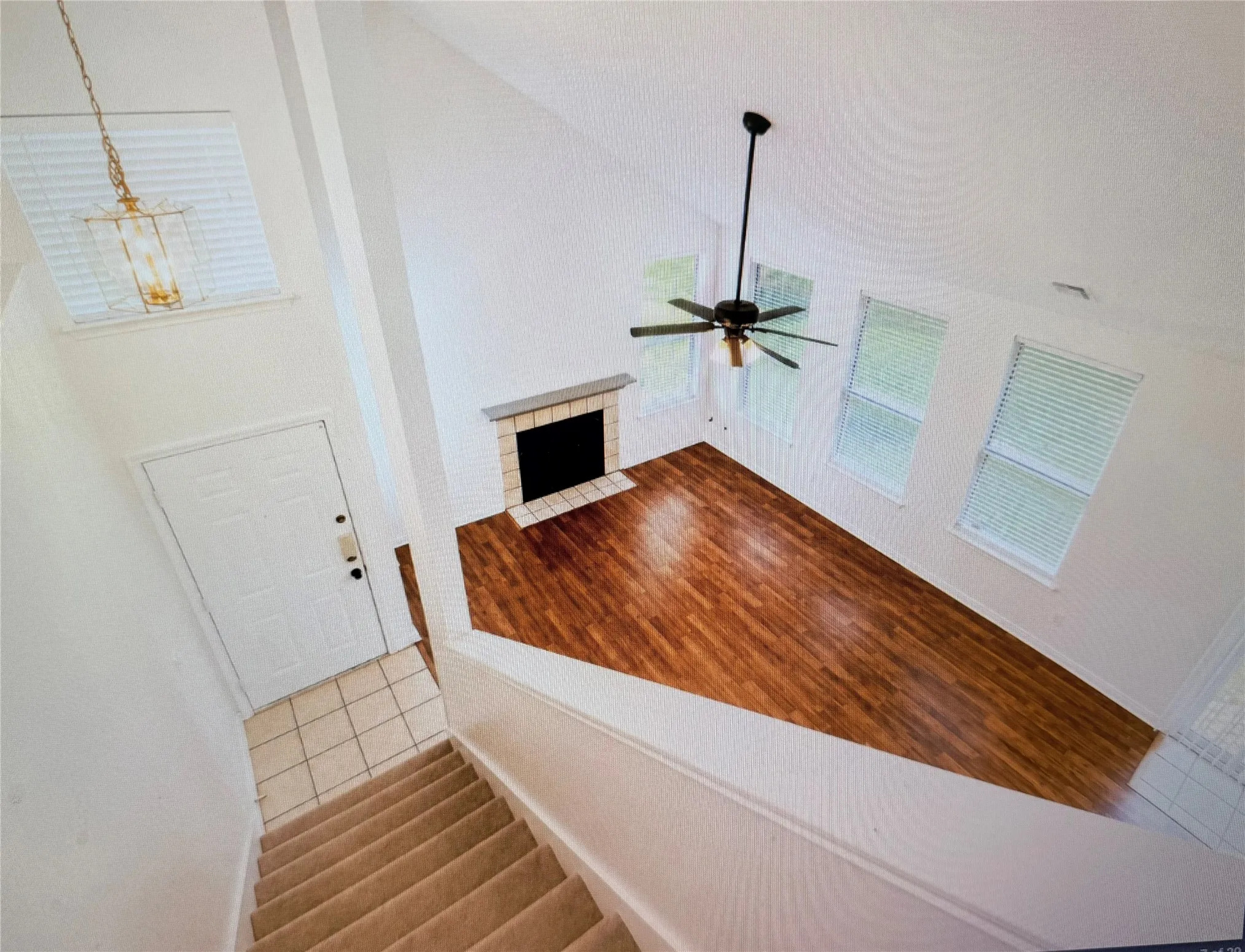 Vaulted ceilings enhance this living area featuring wood-finish flooring, a fireplace with a stone mantel, and multiple windows with blinds