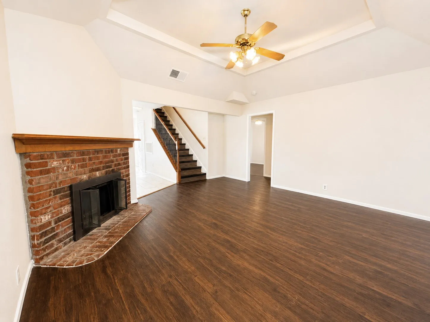 Spacious room featuring rich wood-finish flooring and a brick fireplace with a wood mantel