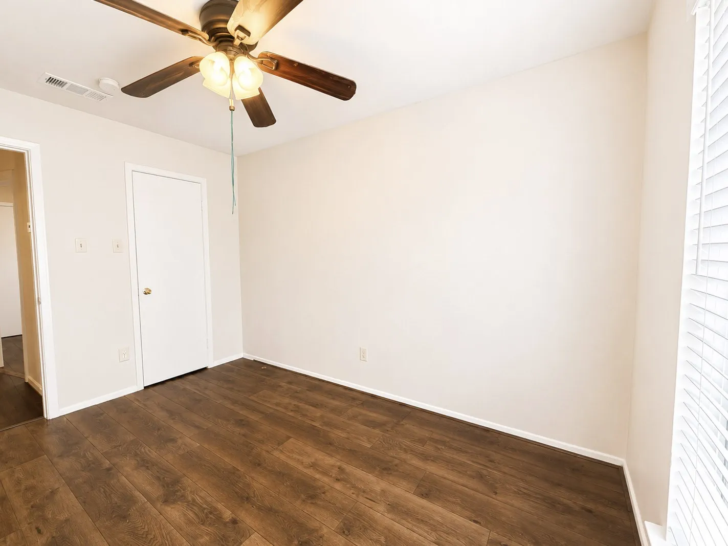Spacious room featuring wood-finish flooring, light-colored walls, and a ceiling fan with integrated lighting