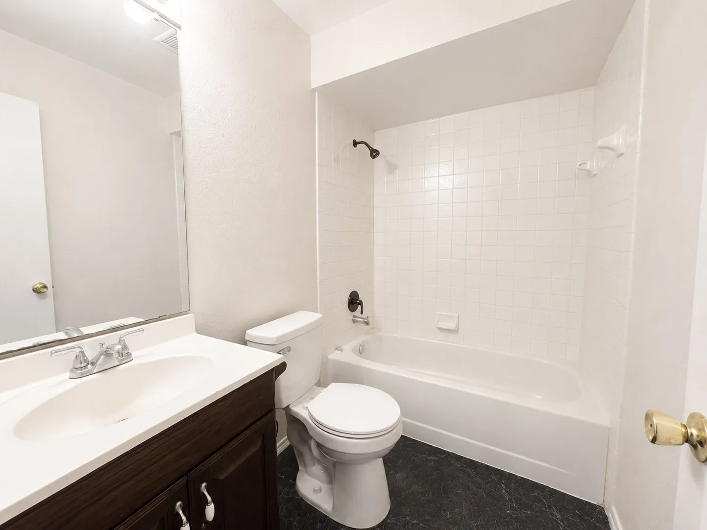 Bathroom featuring a white bathtub, tiled shower surround, a toilet, a vanity with a white countertop and integrated sink, and dark wood-finish cabinetry