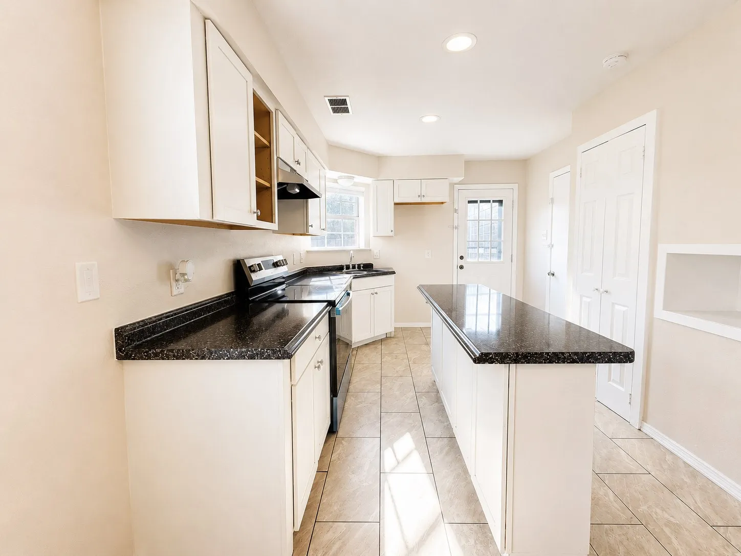 Kitchen featuring L-shaped dark speckled countertops, a central island with matching countertop, white cabinetry, a built-in range, and tile flooring