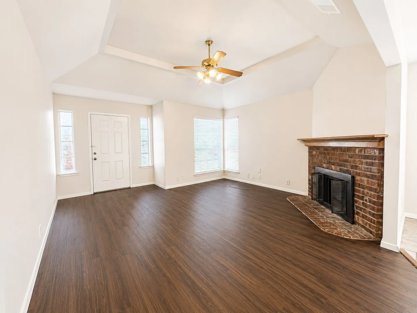 Spacious room featuring vaulted ceilings, wood-finish flooring, and a brick fireplace with a wood mantle