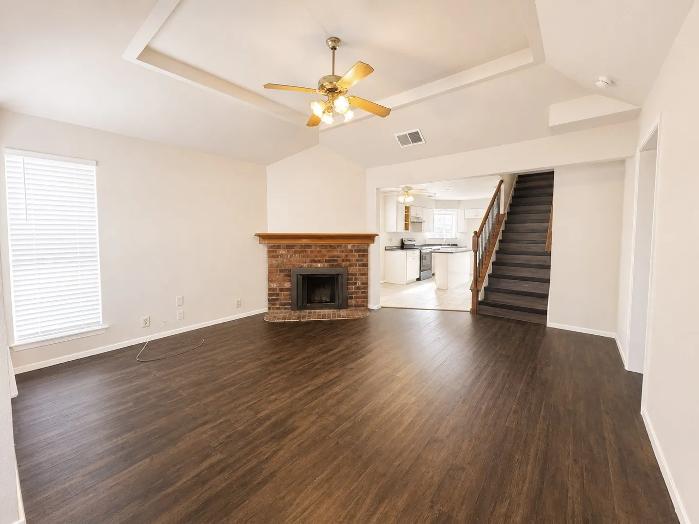 Open-concept living area featuring dark wood-finish flooring, a brick fireplace with a wood mantel, and a vaulted ceiling with a ceiling fan