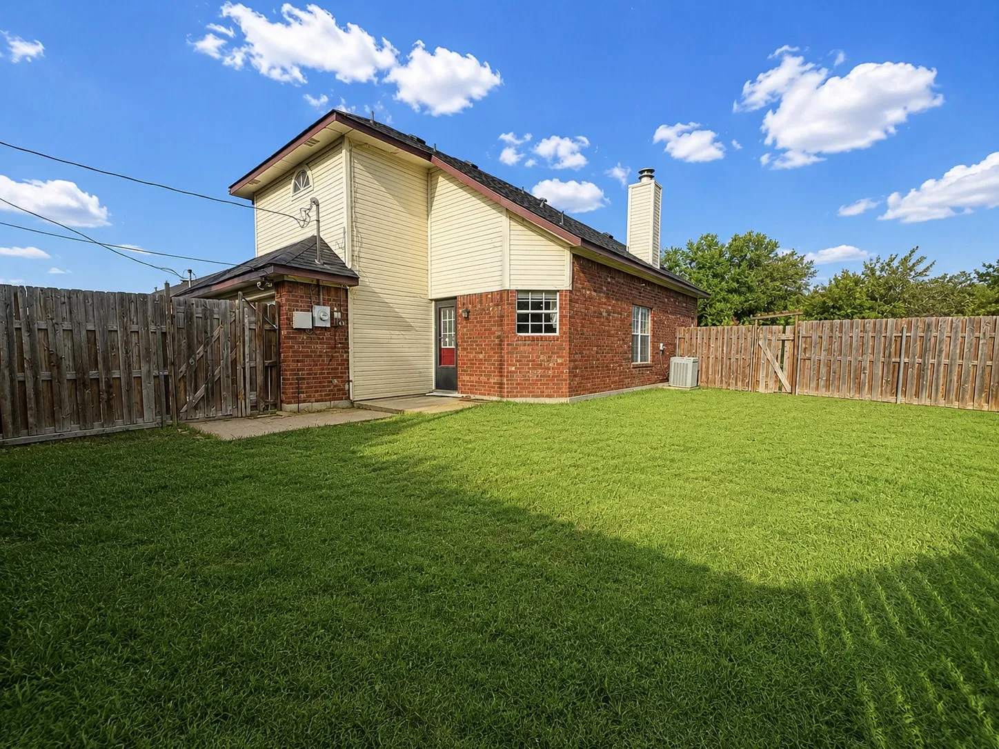 Spacious rear yard with a manicured lawn, full privacy fencing, and a brick and siding exterior