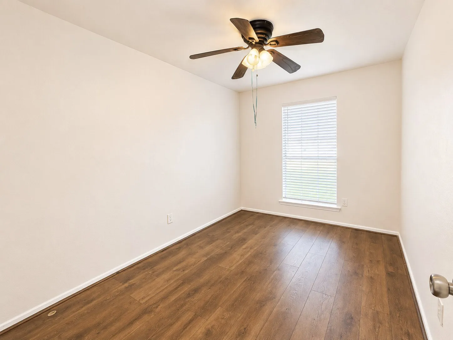 Interior room featuring neutral wall tones, wood-finish flooring, a ceiling fan with integrated lighting, and a window with horizontal blinds