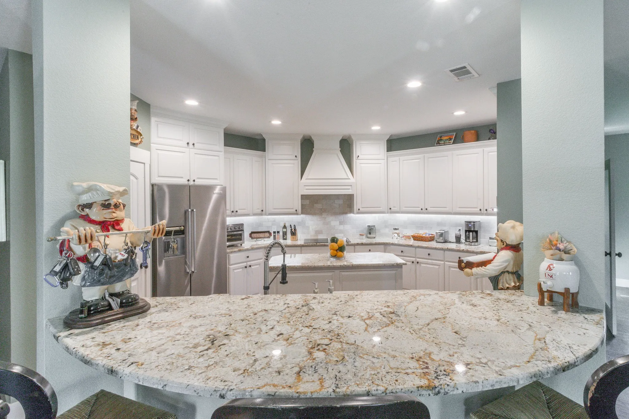 Expansive kitchen featuring a curved peninsula with stone-finish countertops, white shaker cabinetry, stainless steel appliances, and recessed lighting
