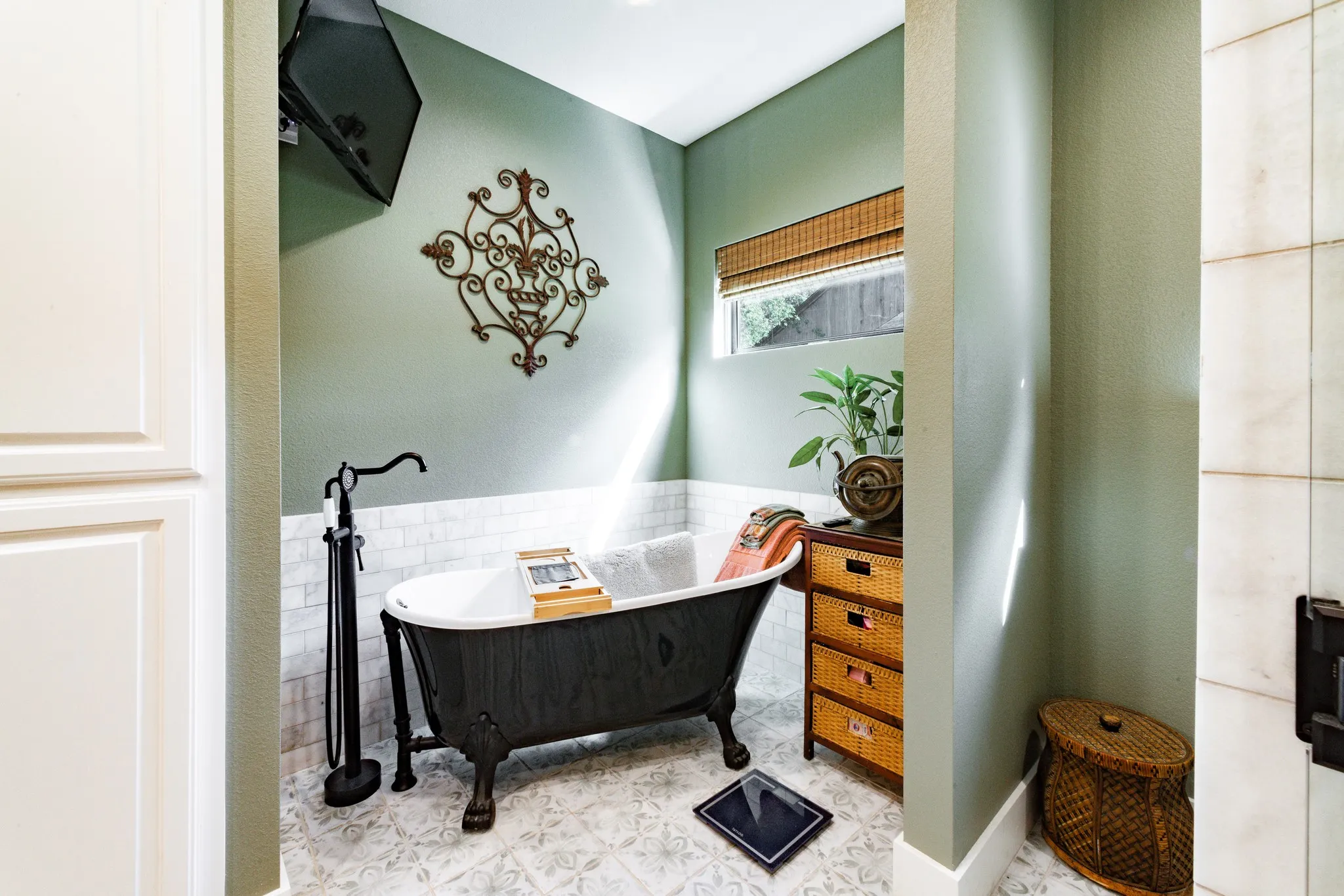 Freestanding clawfoot tub with a matte black floor-mounted faucet, complemented by white subway tile wainscoting and patterned floor tile