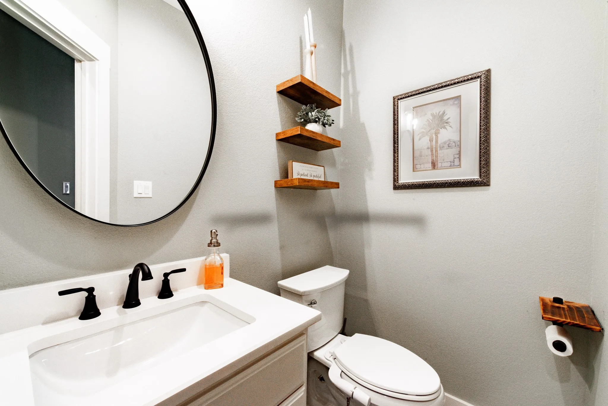 Modern bathroom featuring a white vanity with a rectangular undermount sink, matte black faucet, and a large circular mirror